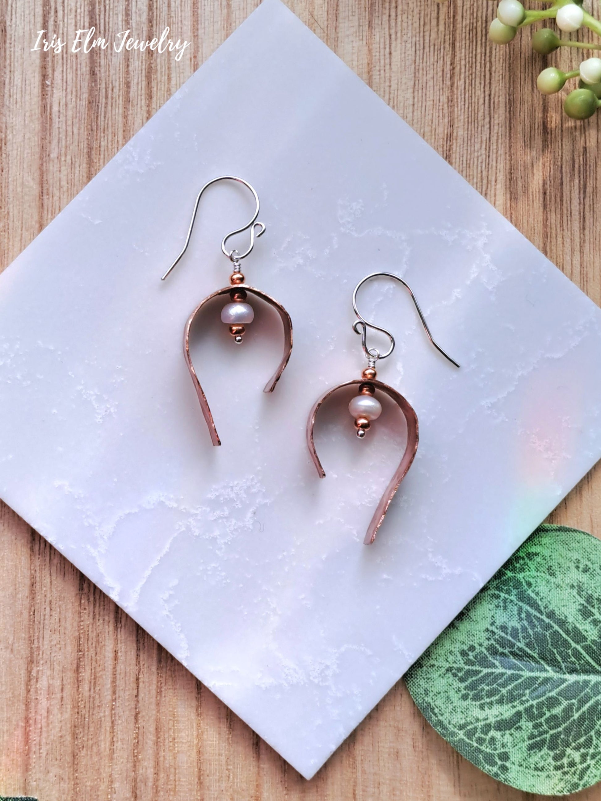 Pair of copper freshwater pearl earrings on a white tile with a wooden background