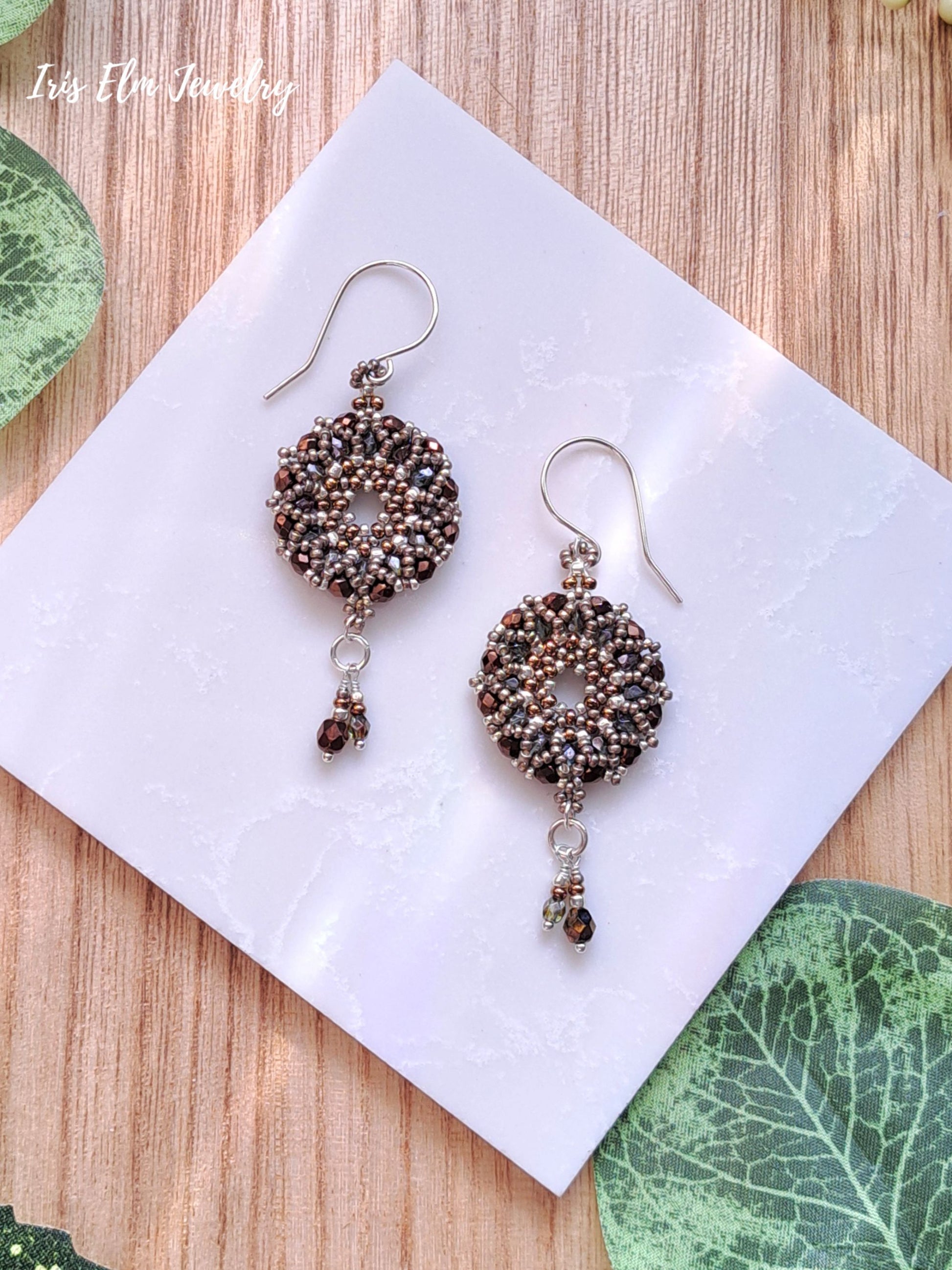 Pair of beaded brown Czech glass woven circle wreath earrings on a white card with green leaves in the background