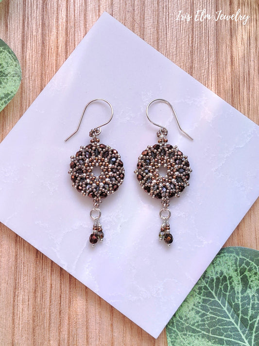 Pair of beaded brown glass wreath earrings on a white card with green leaves in the background