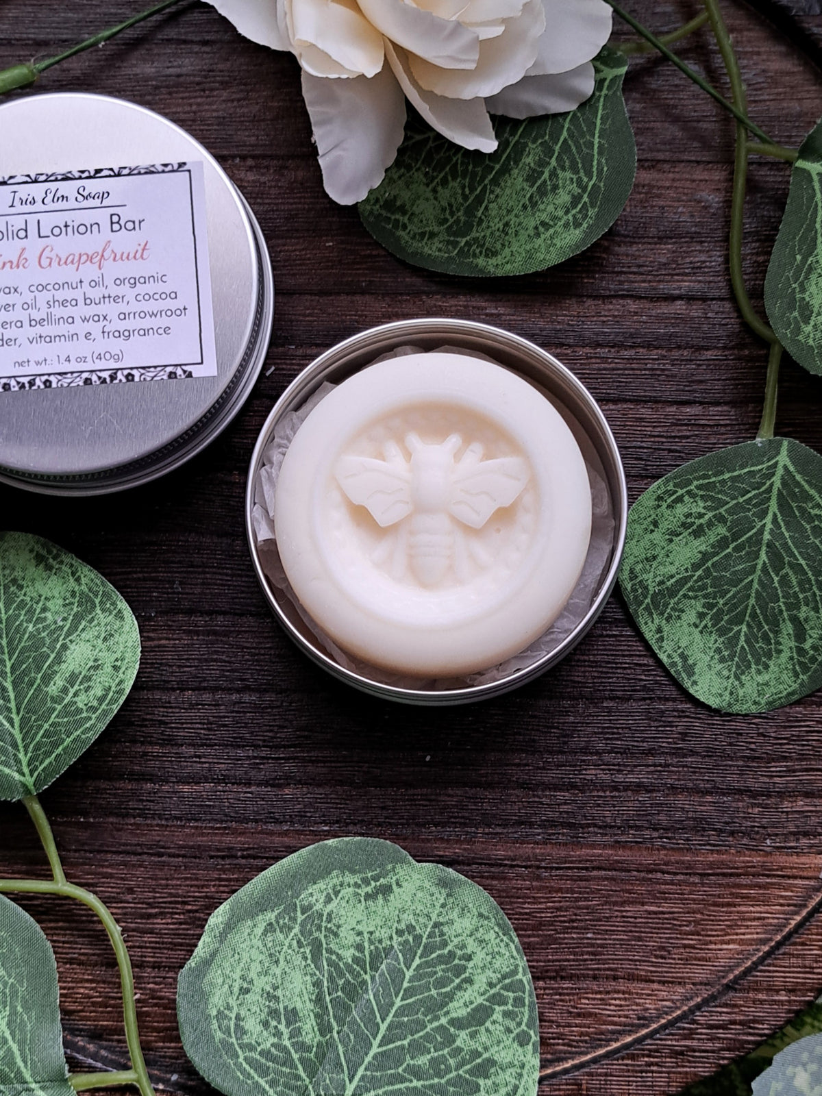 Solid lotion bar in a tin with green leaves and flowers on a wooden surface