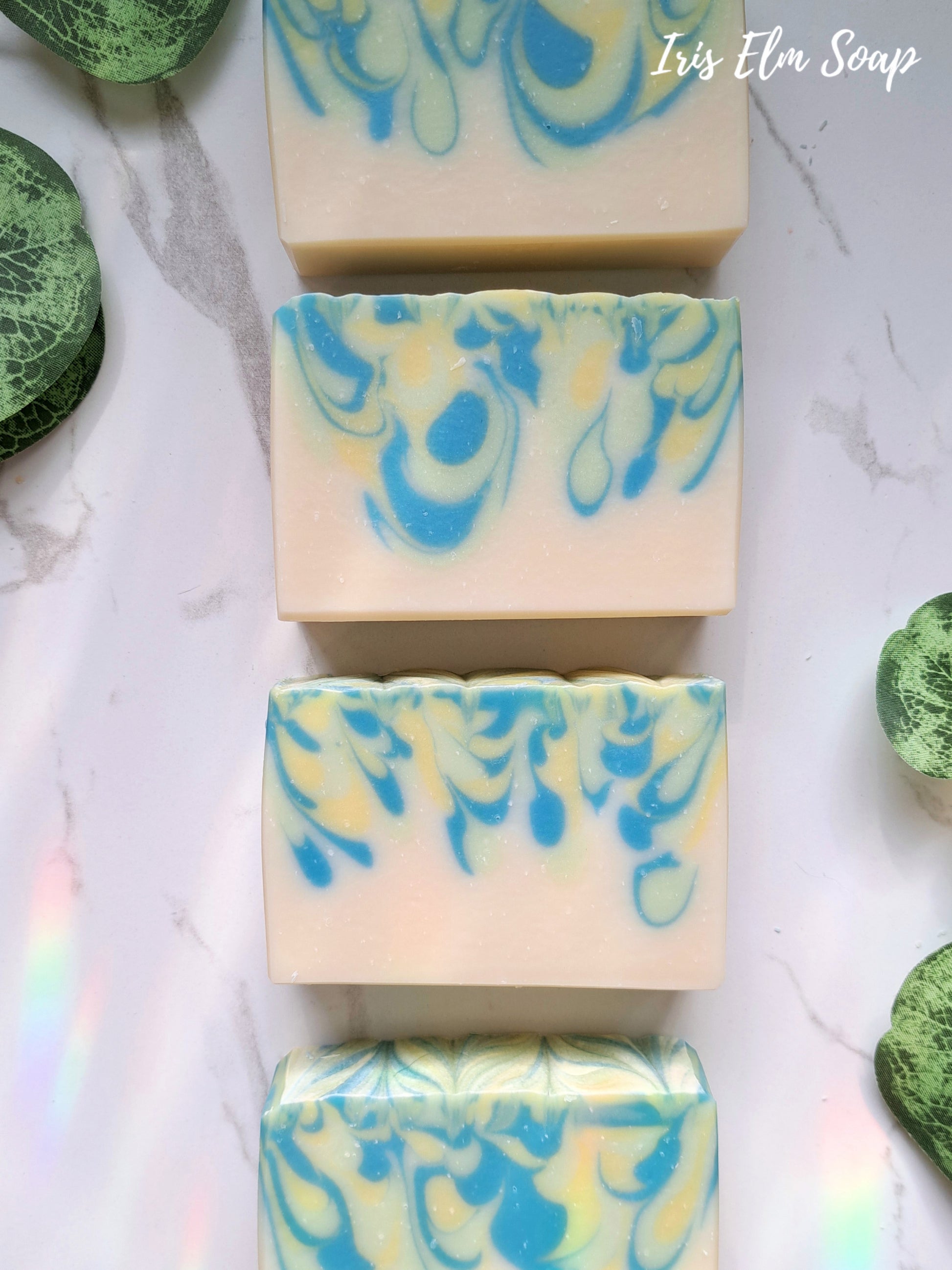 Marbled white tea and ginger handmade soap bars with blue and green swirls on a marble surface, featuring 'Iris Elm Soap' branding.