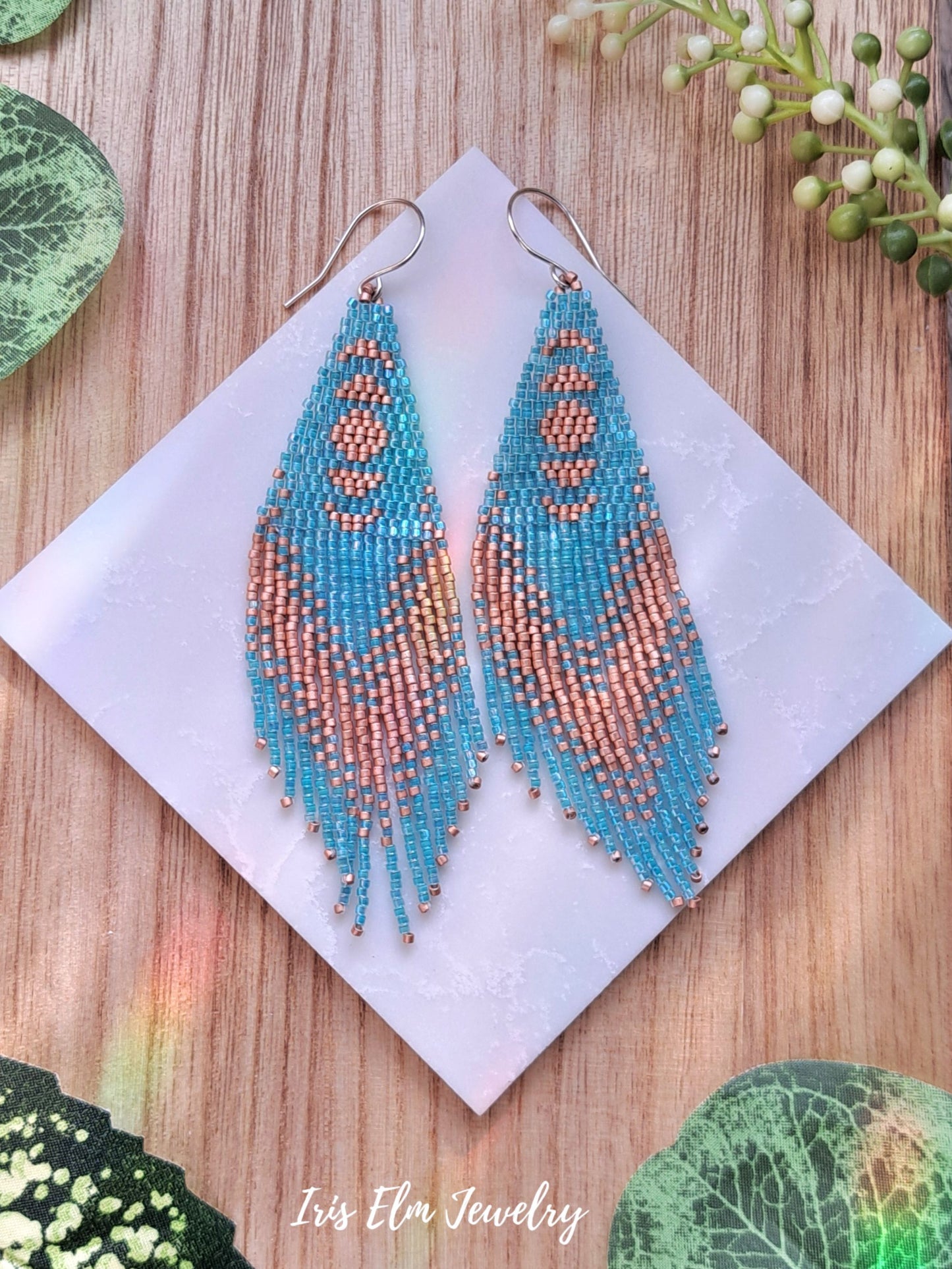 aqua blue and copper peach moon phase seed bead fringe beaded earrings on a white card with green leaves around