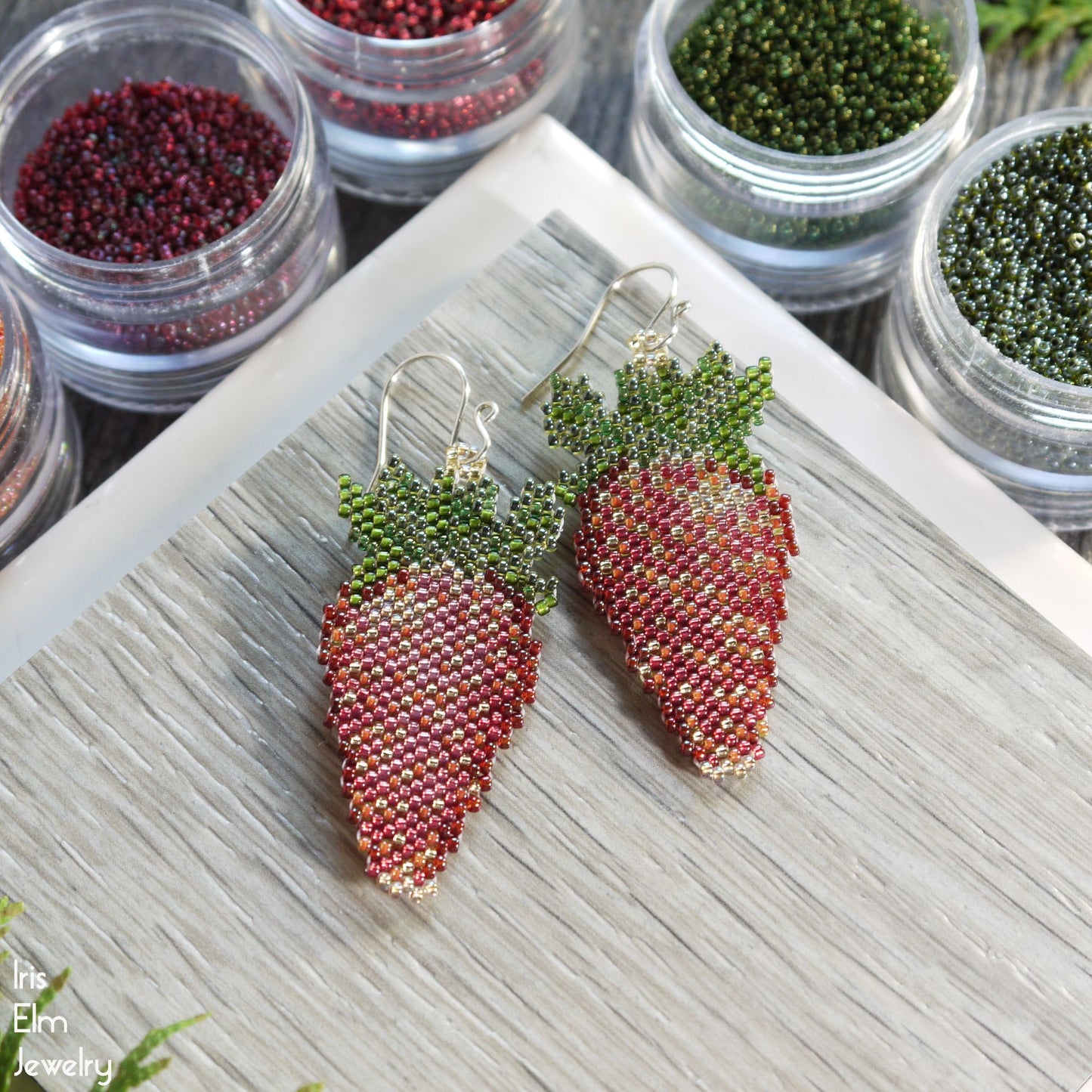 strawberry-shaped beaded earrings on a wooden surface with small containers of beads in the background.
