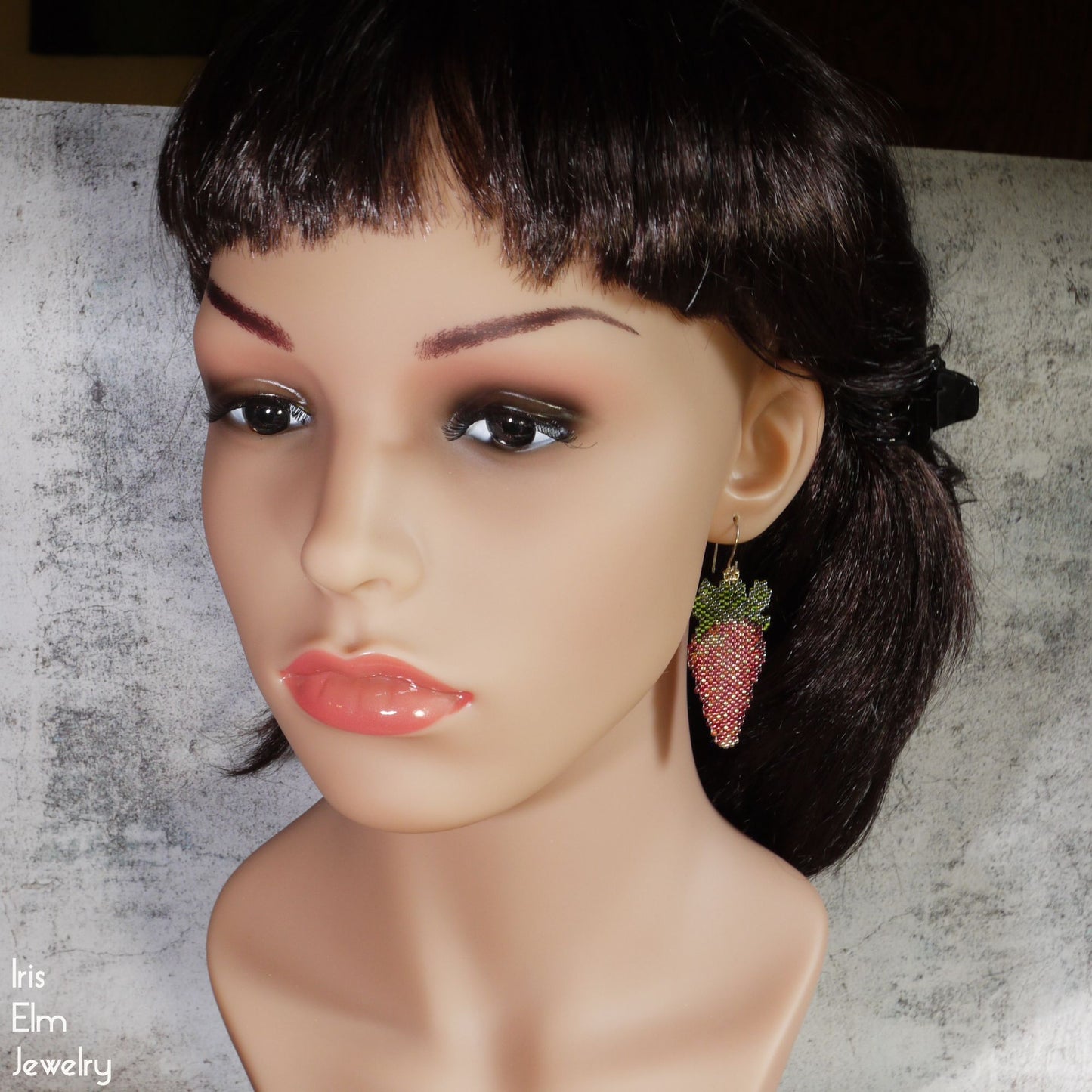Mannequin head with strawberry earrings on a textured background