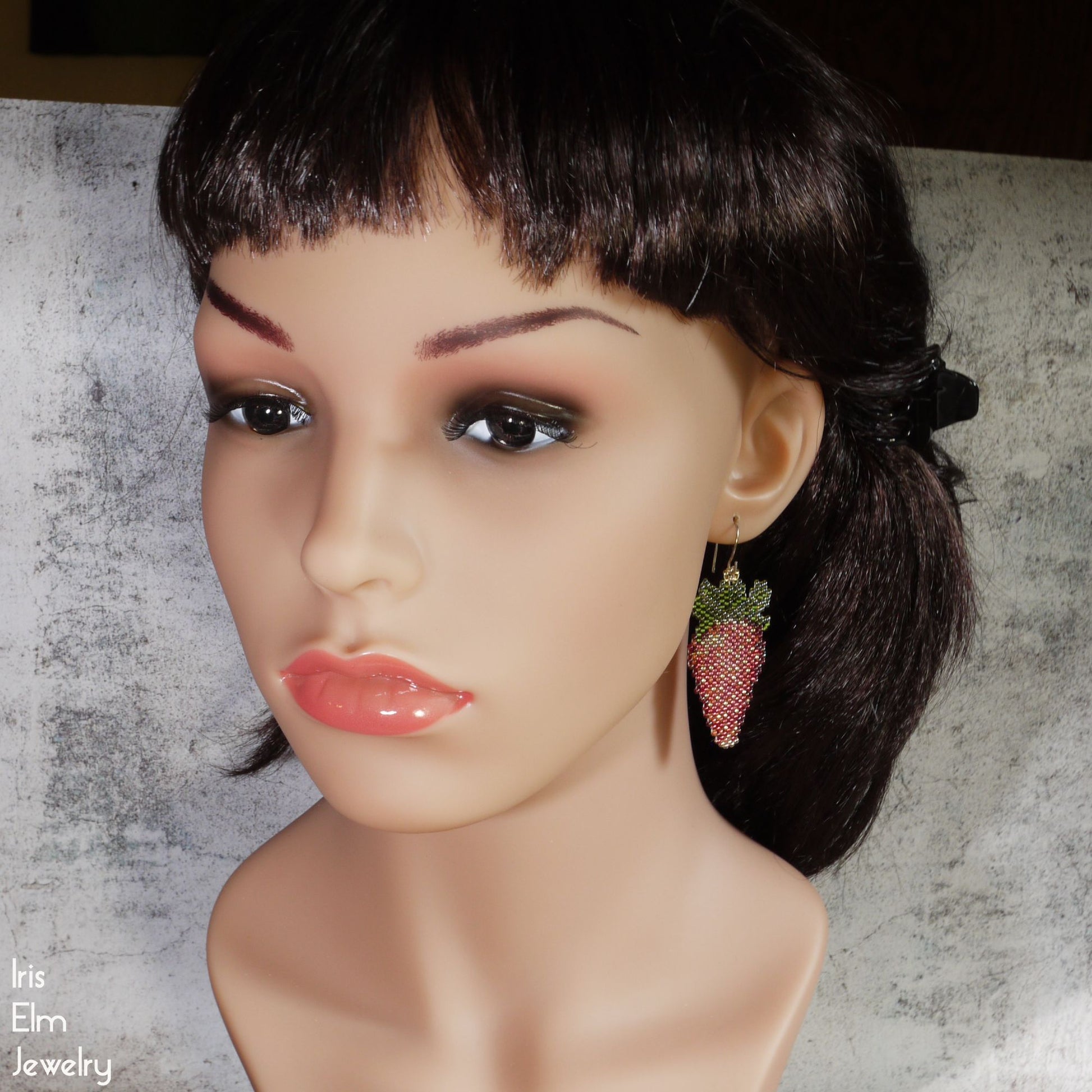 Mannequin head with strawberry earrings on a textured background