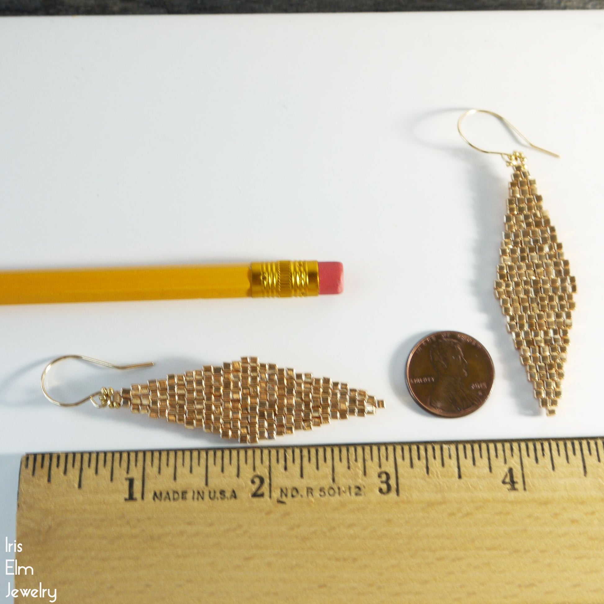 2 and 7/8 inch long Gold diamond shape earrings with a pencil and penny for scale on a white background, Iris Elm Jewelry branding visible.