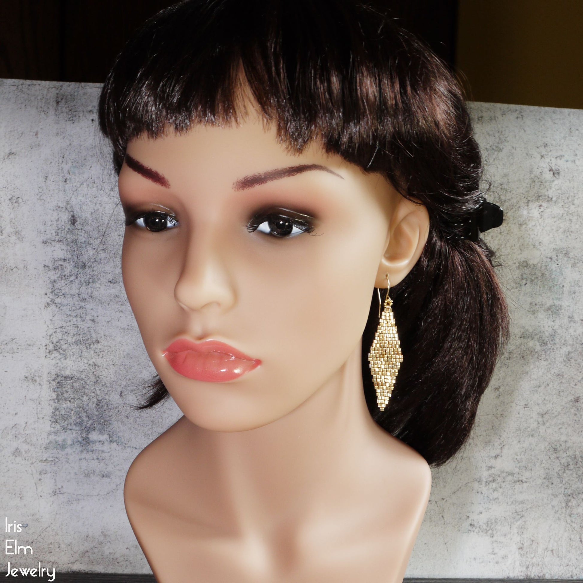 Mannequin head with a wig and long gold earrings on a textured surface