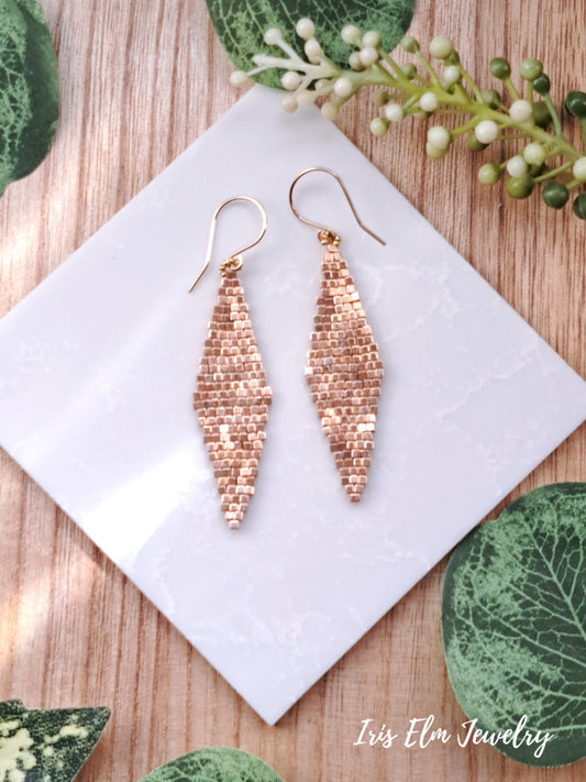 beadwork gold glass diamond shape long earrings on a white card with green leaves in the background