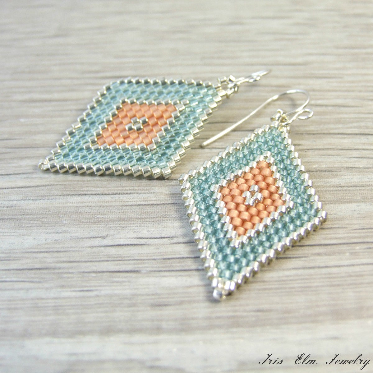 Pair of handmade beaded peach and aqua southwestern earrings with geometric design on a wooden surface, branded 'Iris Elm Jewelry'.