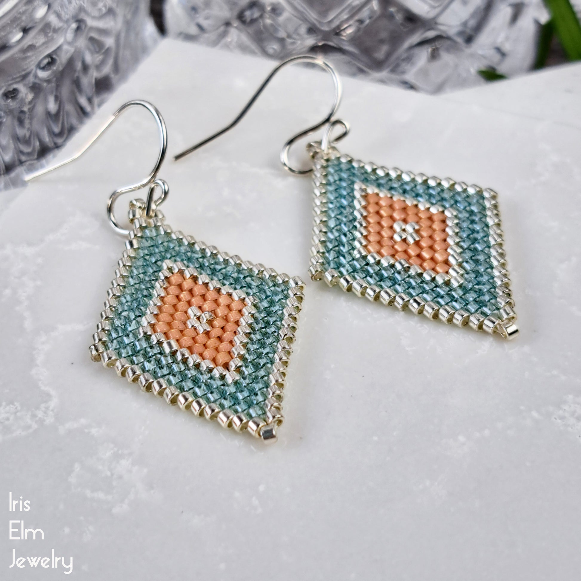 Pair of beaded seed bead earrings with geometric southwestern design on a white surface, featuring the brand 'Iris Elm Jewelry'.