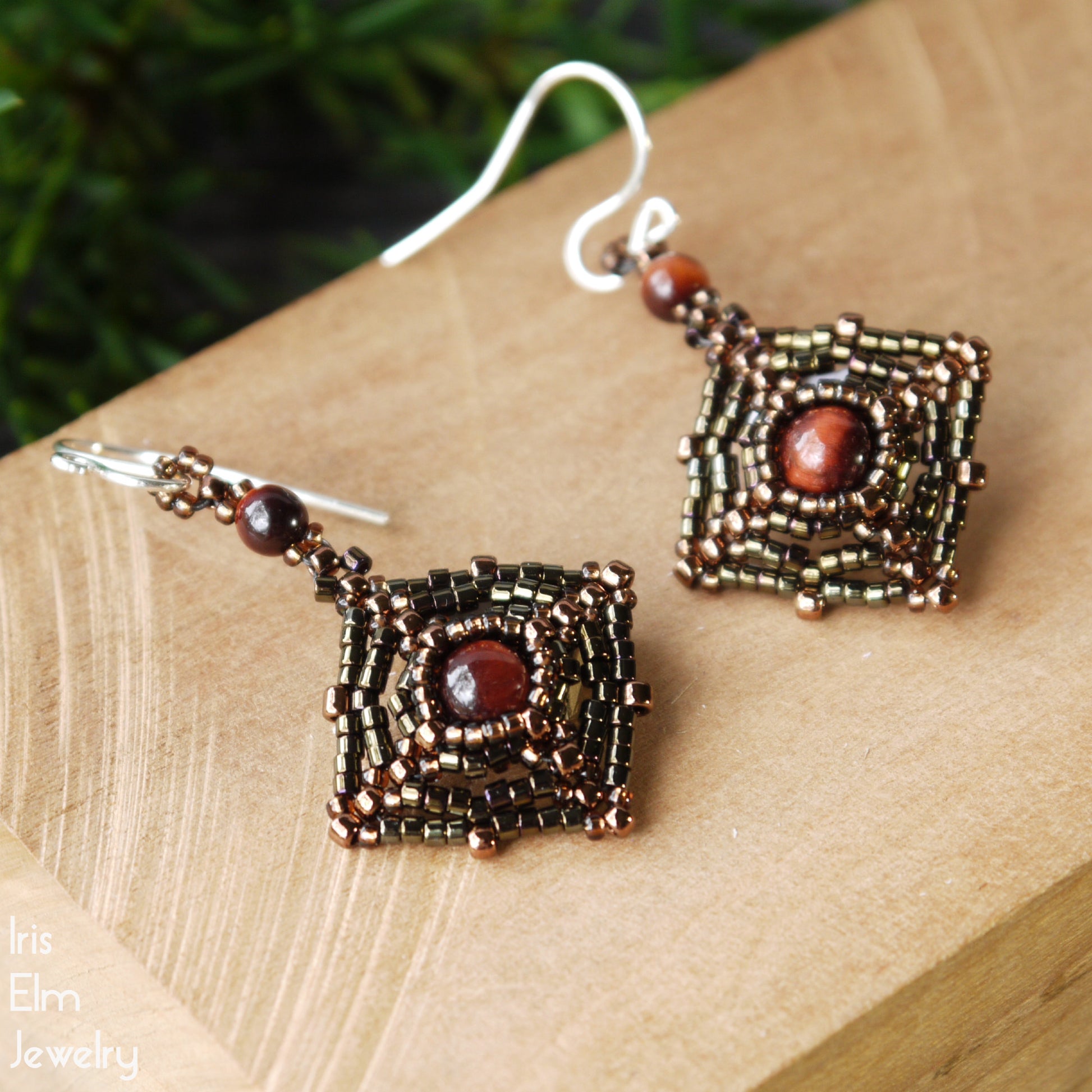 Beaded square woven earrings with reddish brown gemstones on a wooden surface, branded 'Iris Elm Jewelry'.
