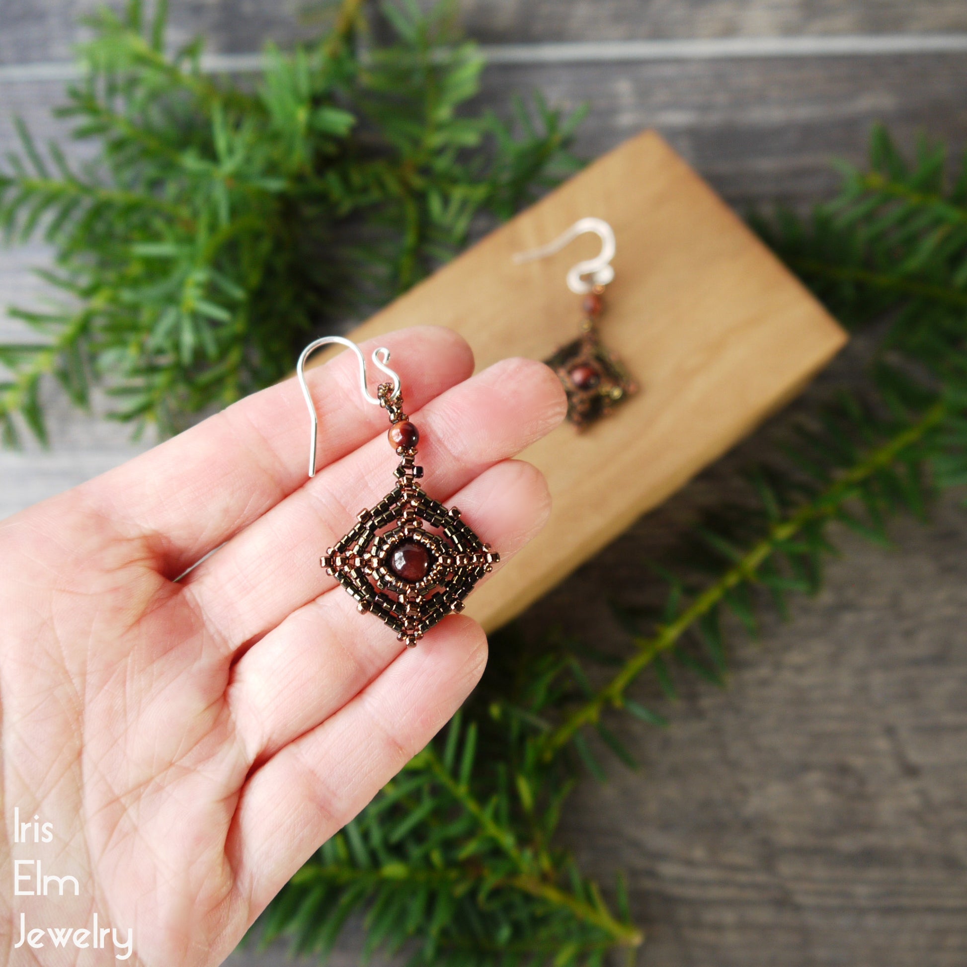 Hand holding a pair of ornate red tiger eye stone and seed bead earrings with a natural background