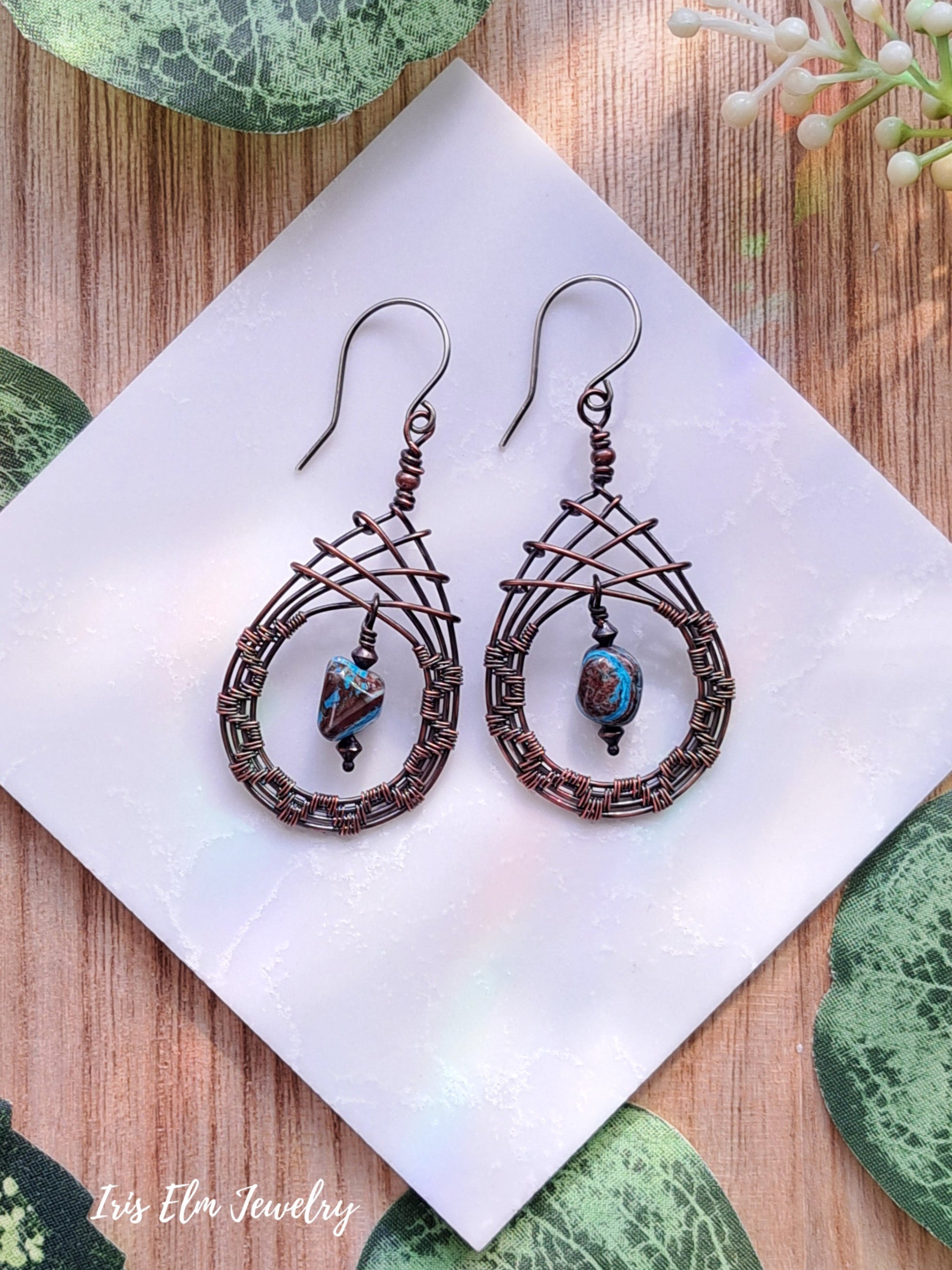 Pair of copper wire-wrapped blue sky jasper teardrop earrings with beads on a white napkin.