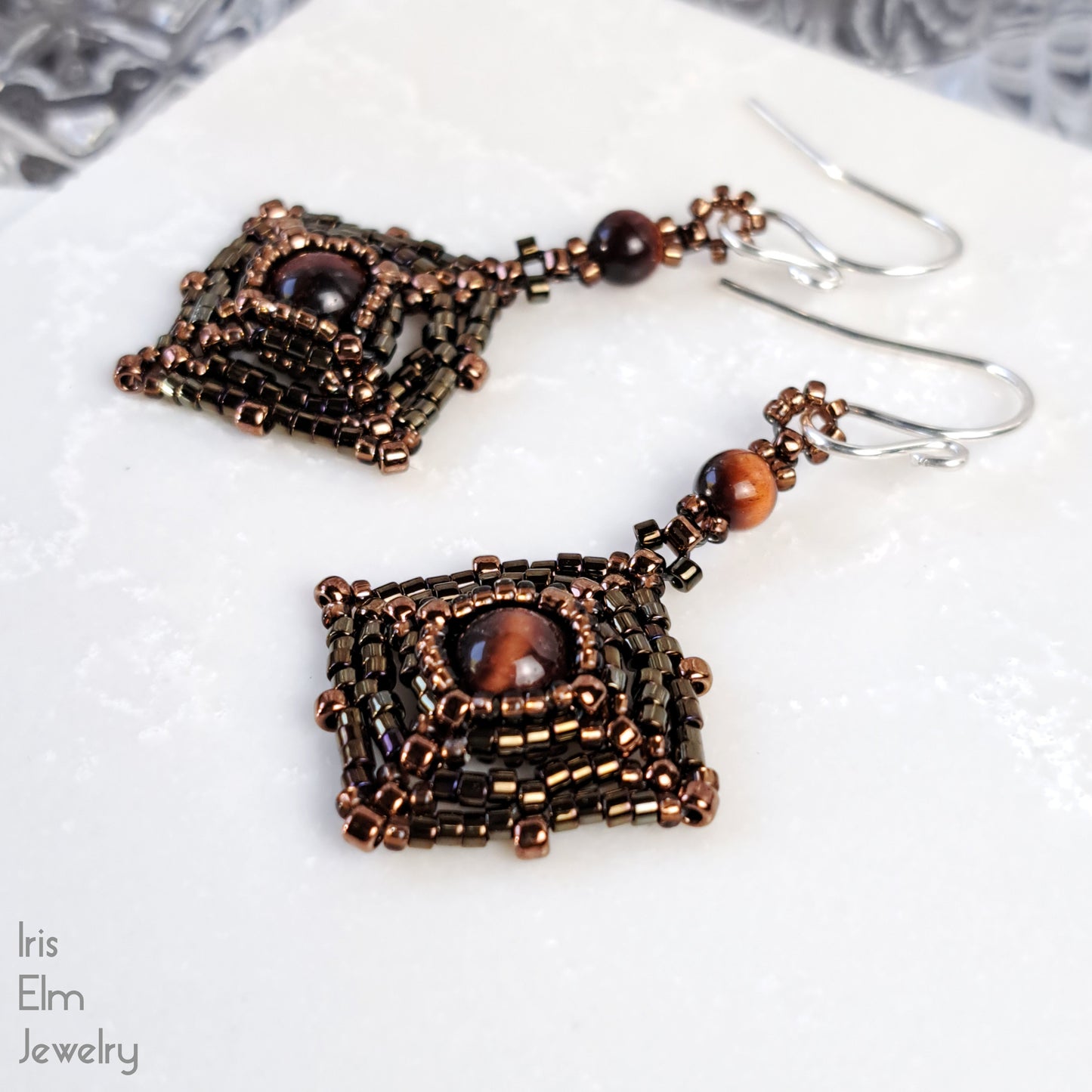 Pair of beaded earrings with brown red tiger eye stones on a white surface, branded 'Iris Elm Jewelry'.