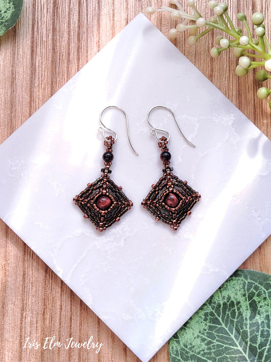 Pair of decorative brown red tiger eye stone and seed bead earrings on a white tile with a wooden background
