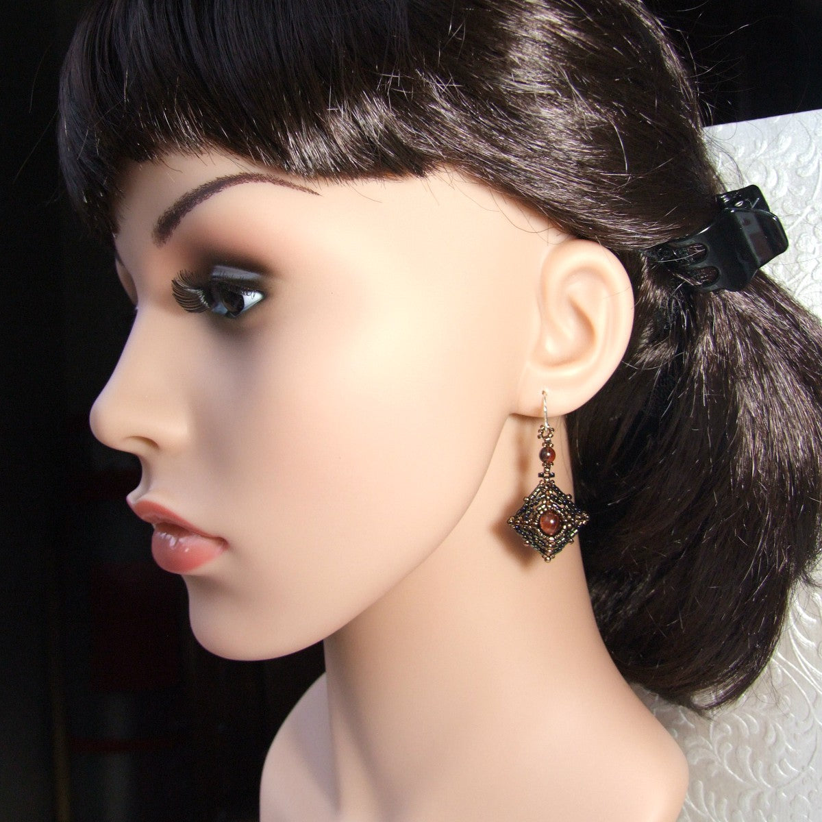 Mannequin head with dark hair styled in a ponytail and wearing a red tiger eye beaded earring.