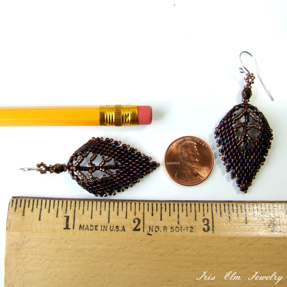 Pair of beaded glass leaf earrings next to a pencil and penny for scale, with 'Iris Elm Jewelry' branding.
