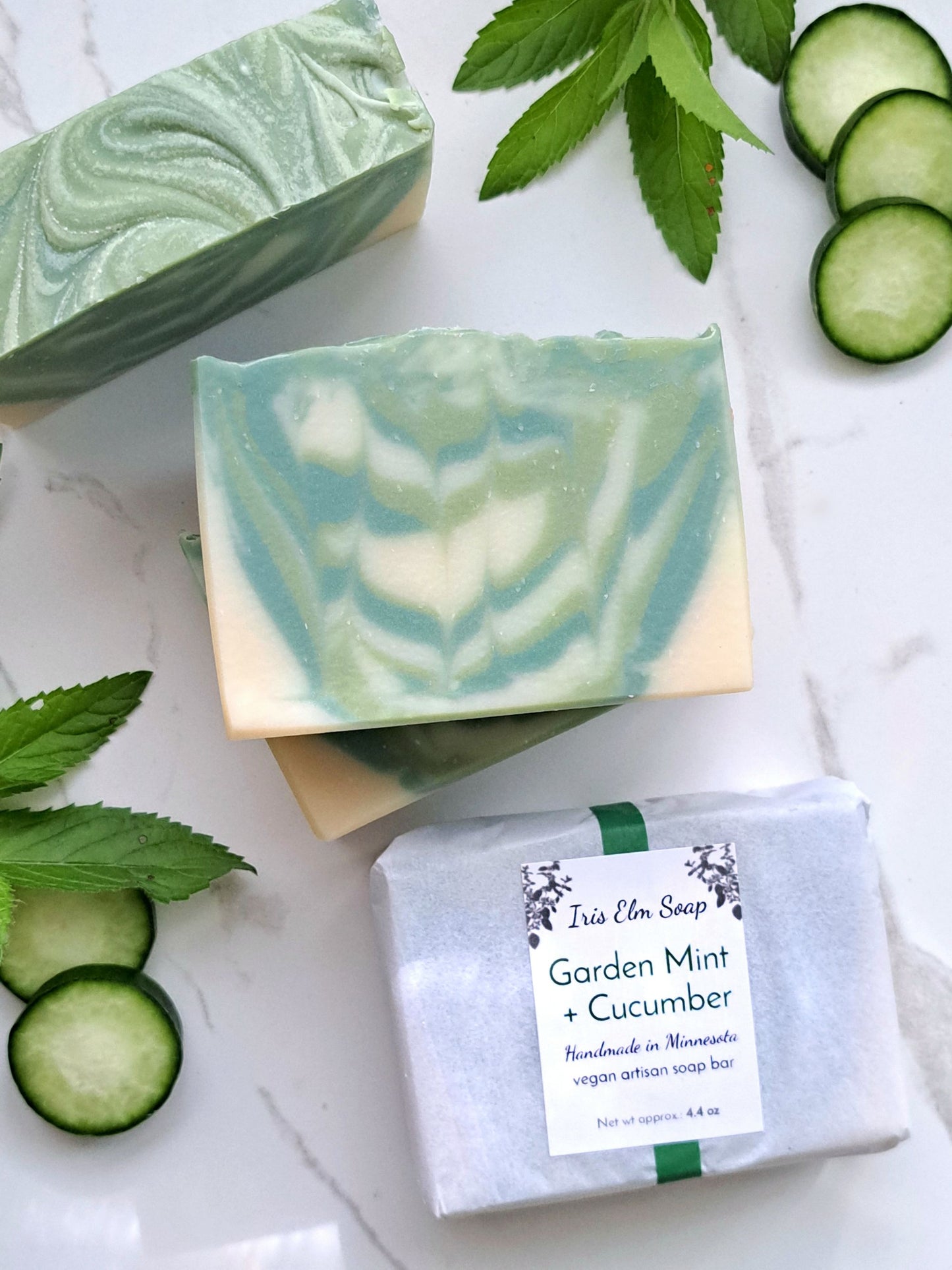 Green and white swirled soap bars with a box labeled 'Garden Mint + Cucumber' on a white background.