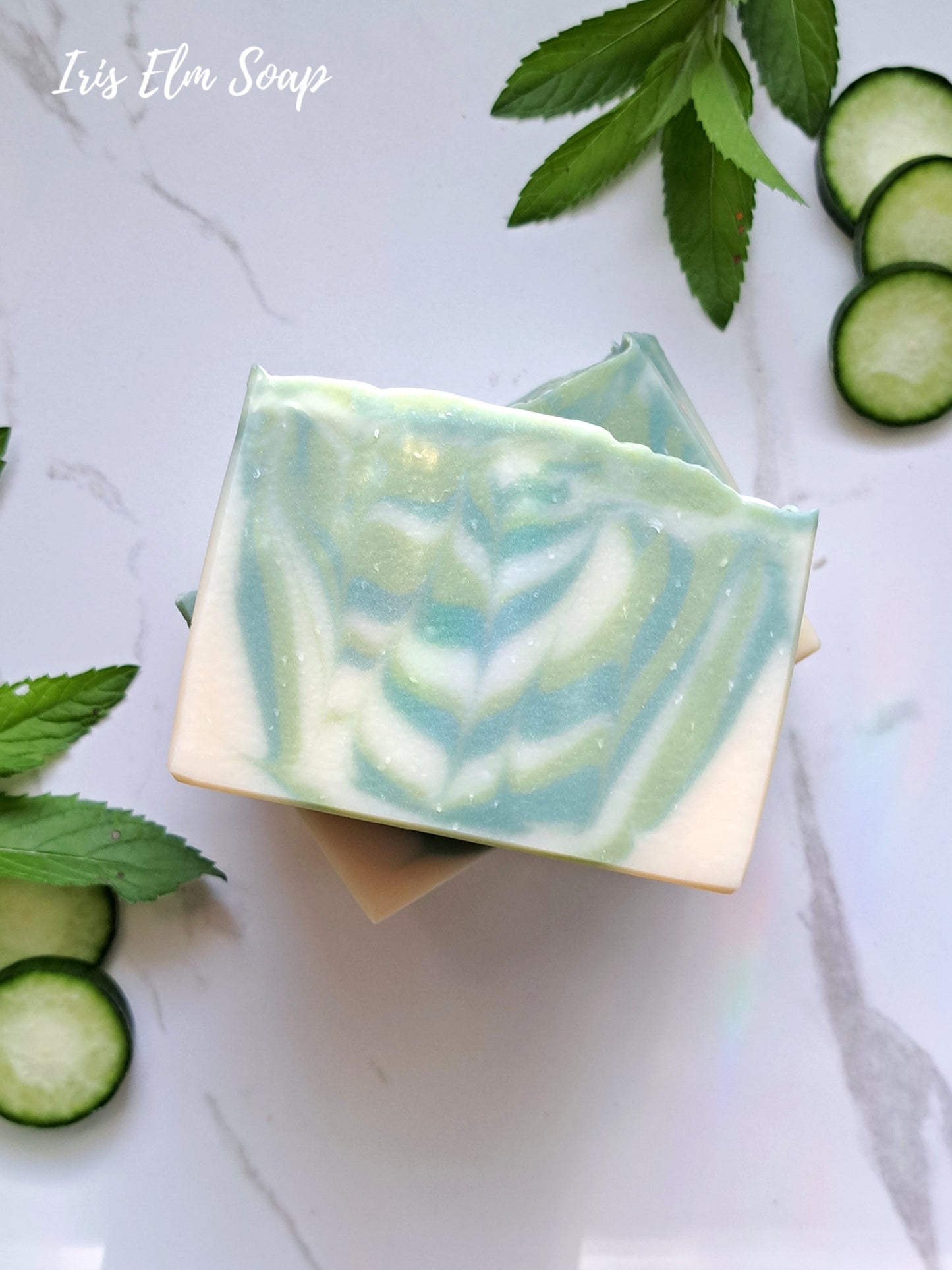 Green and white striped garden mint and cucumber handmade soap bar with cucumber slices and leaves on a light background