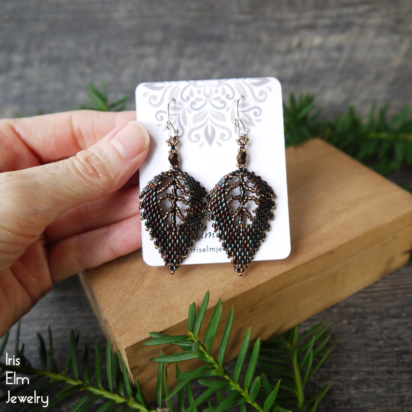 dark brown glass beadwork Leaf-shaped earrings on a card held by a hand with a natural background