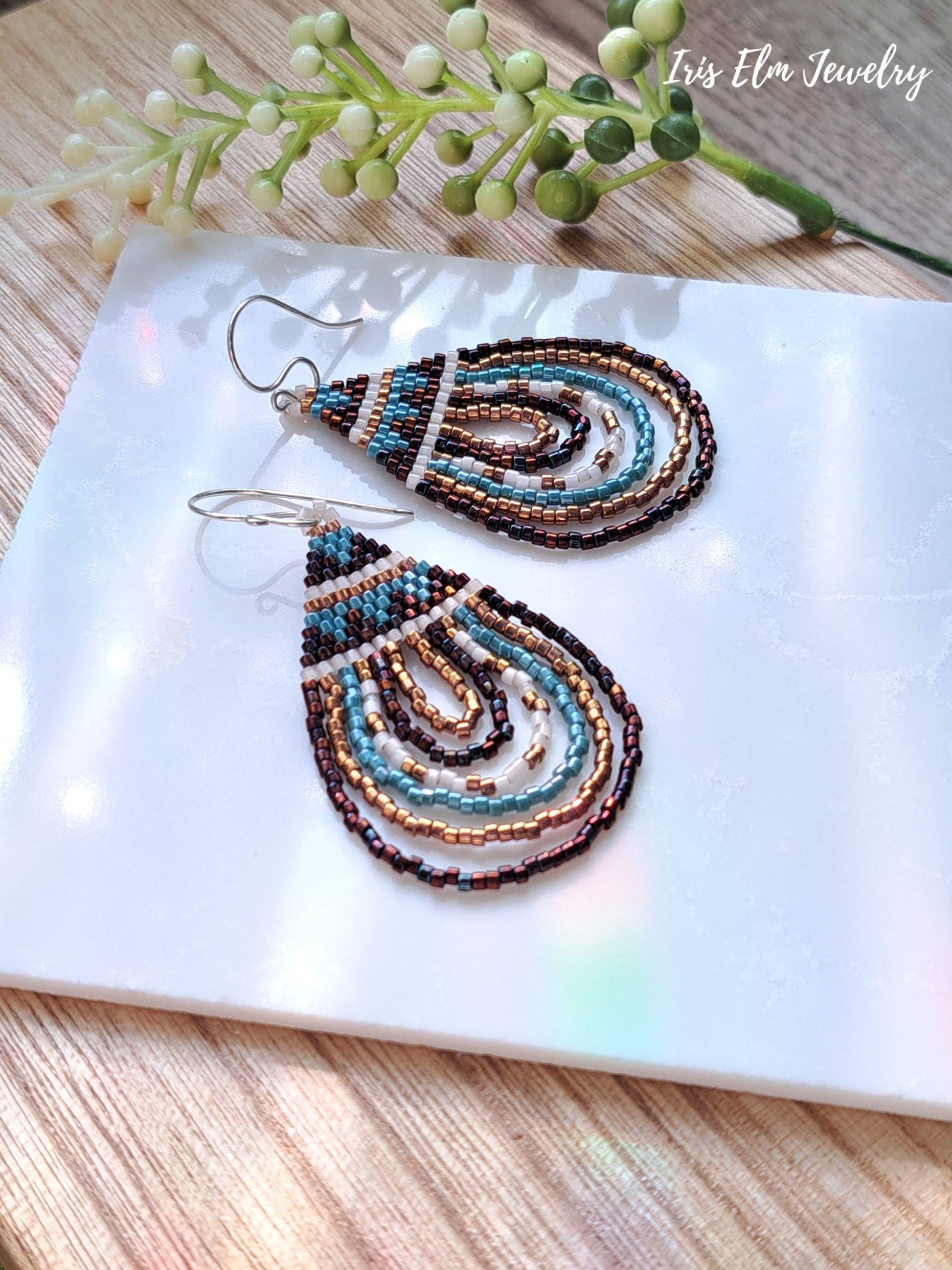 Beaded brown bronze and aqua seed bead teardrop earrings on a white card with 'Iris Elm Jewelry' branding, on a wooden surface.