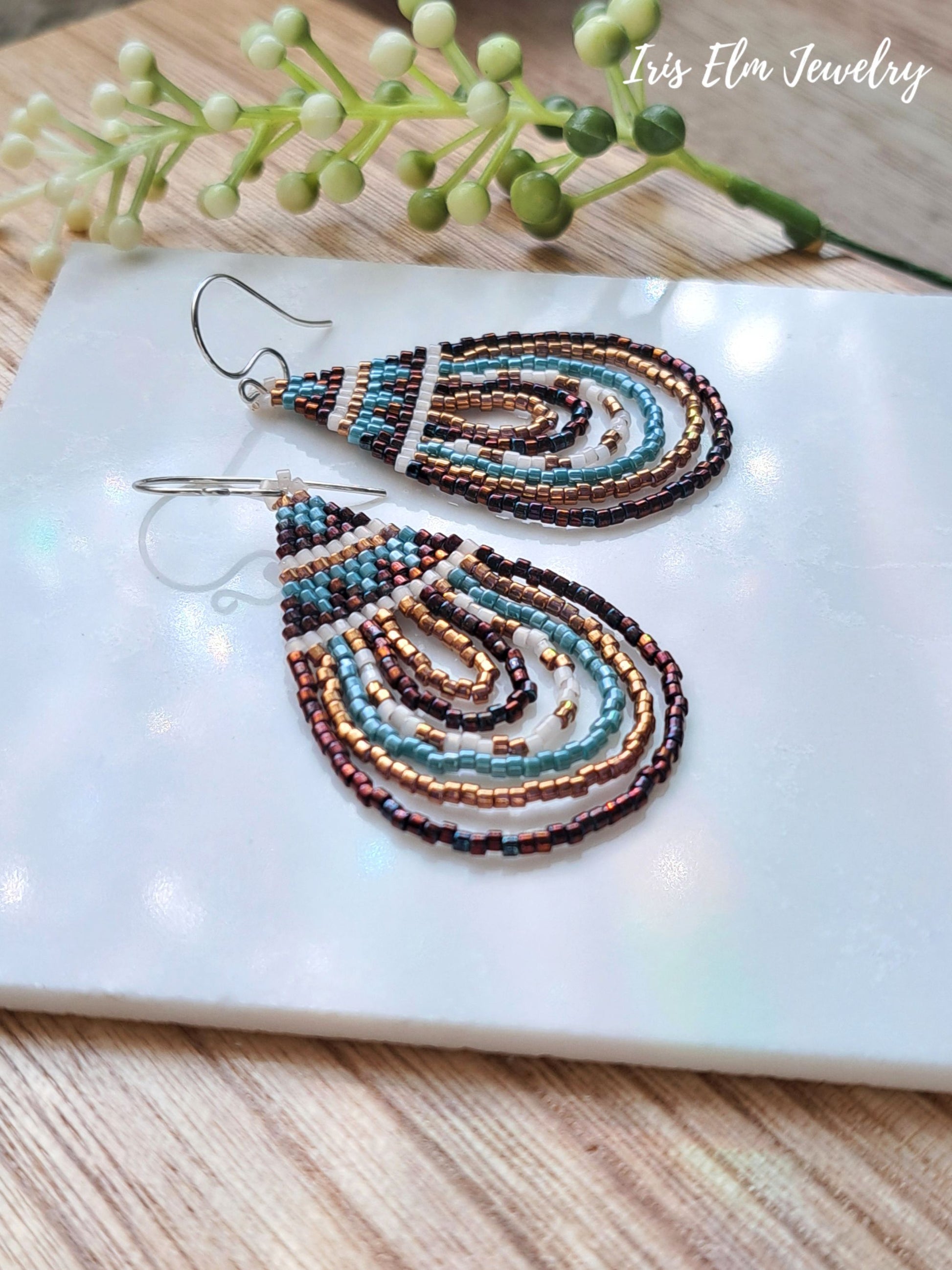 Pair of beaded seed bead bronze and aqua blue teardrop earrings on a white surface with a wooden background
