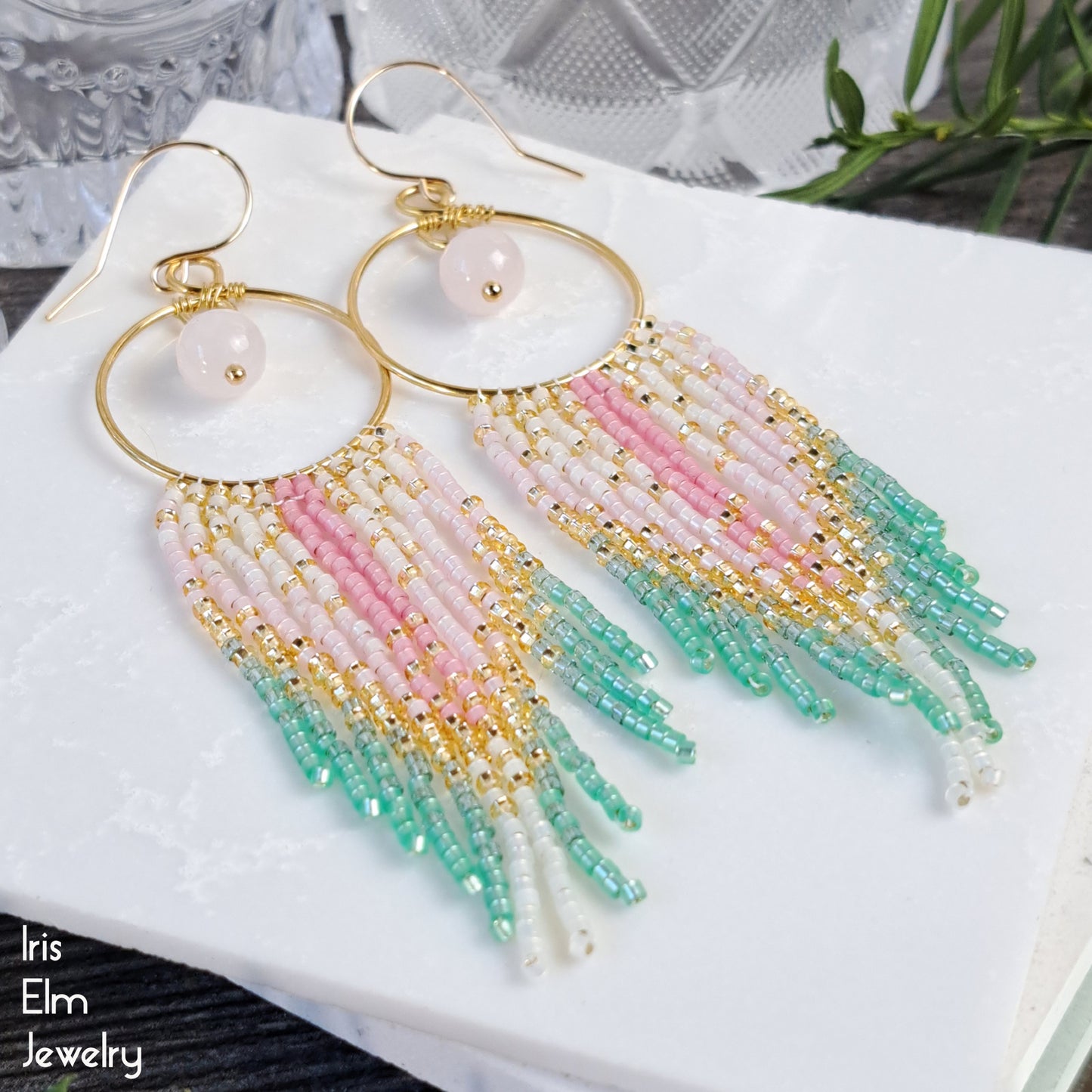 Colorful pink fringe beaded brass hoop earrings on a white surface with 'Iris Elm Jewelry' branding.