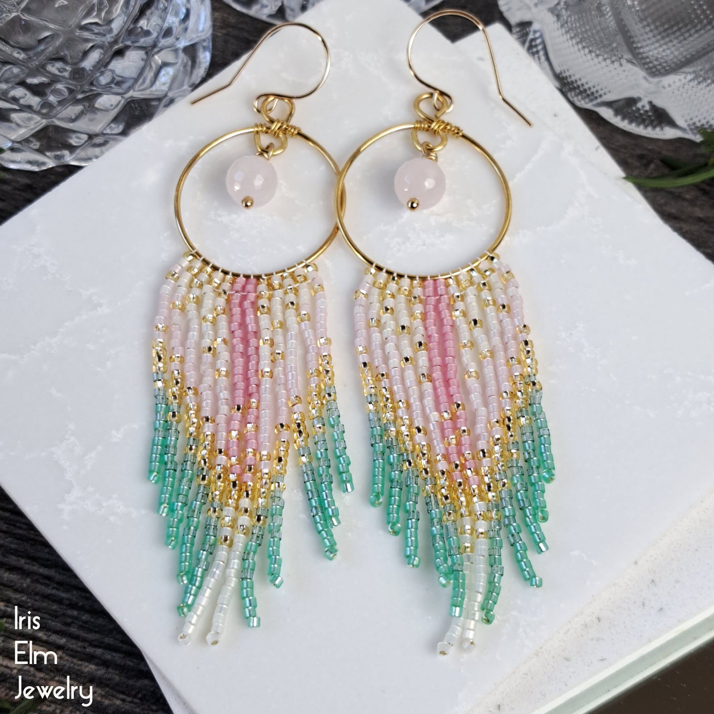 Beaded pink quartz hoop earrings with colorful pink and green fringe on a white surface, branded 'Iris Elm Jewelry'.