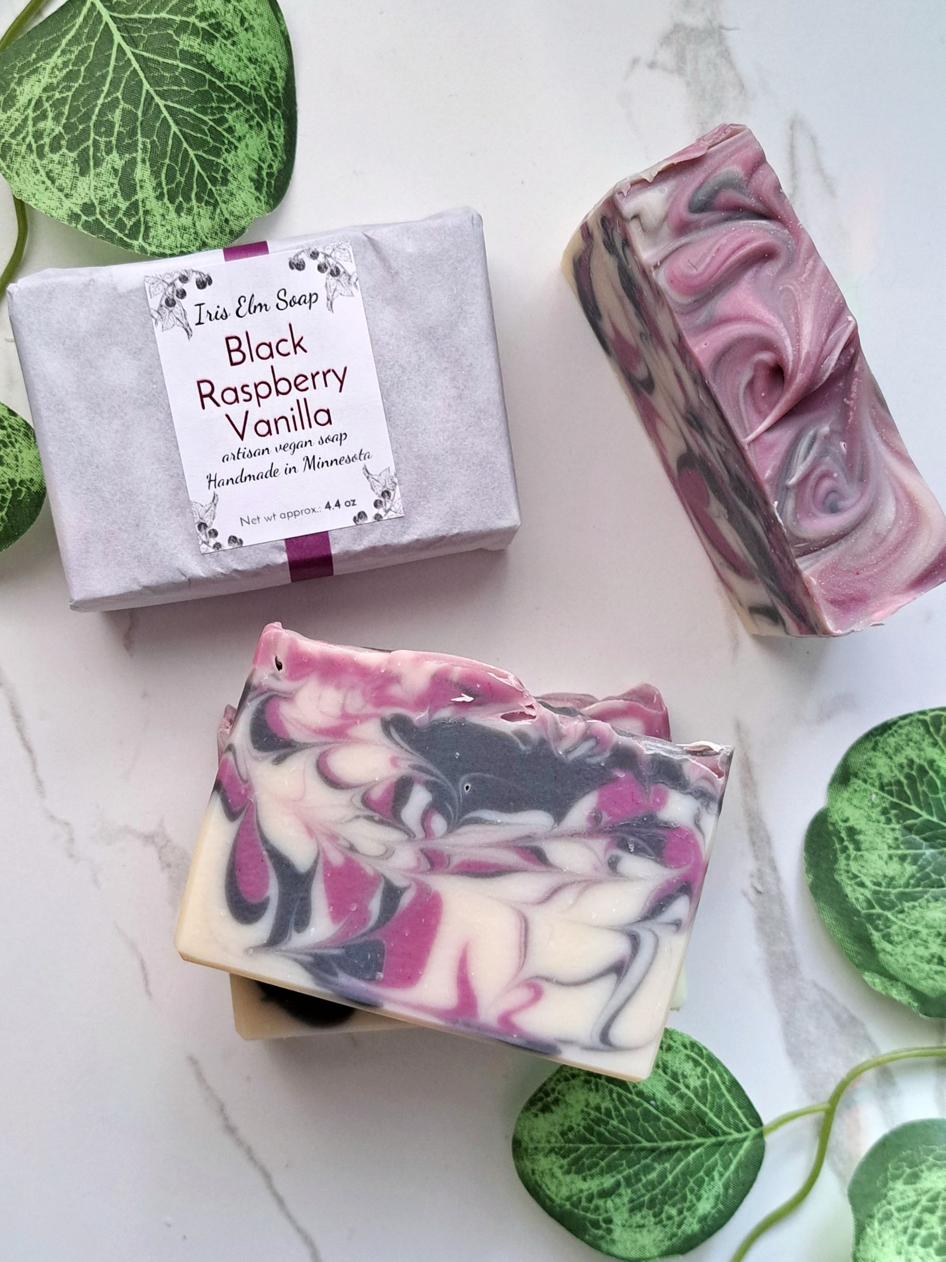 Handmade soap bars with black raspberry vanilla scent on a white surface with green leaves.