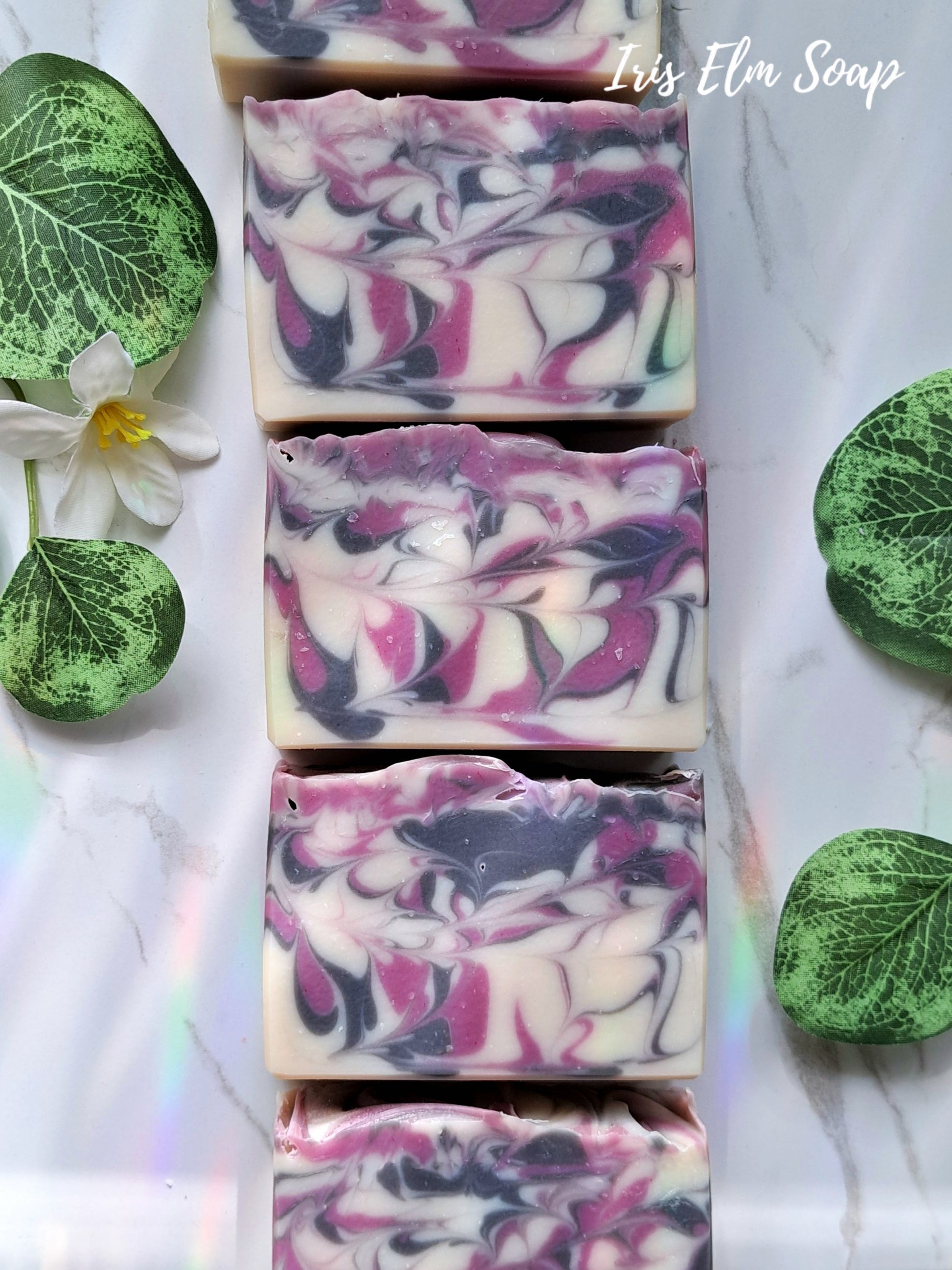 Swirl-patterned black raspberry vanilla handmade soap bars with green leaves and a flower on a light background, branded 'Iris Elm Soap'.
