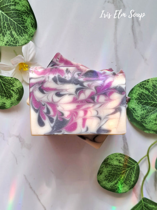 Swirled black raspberry vanilla handmade soap bar with pink and purple on a white background with green leaves