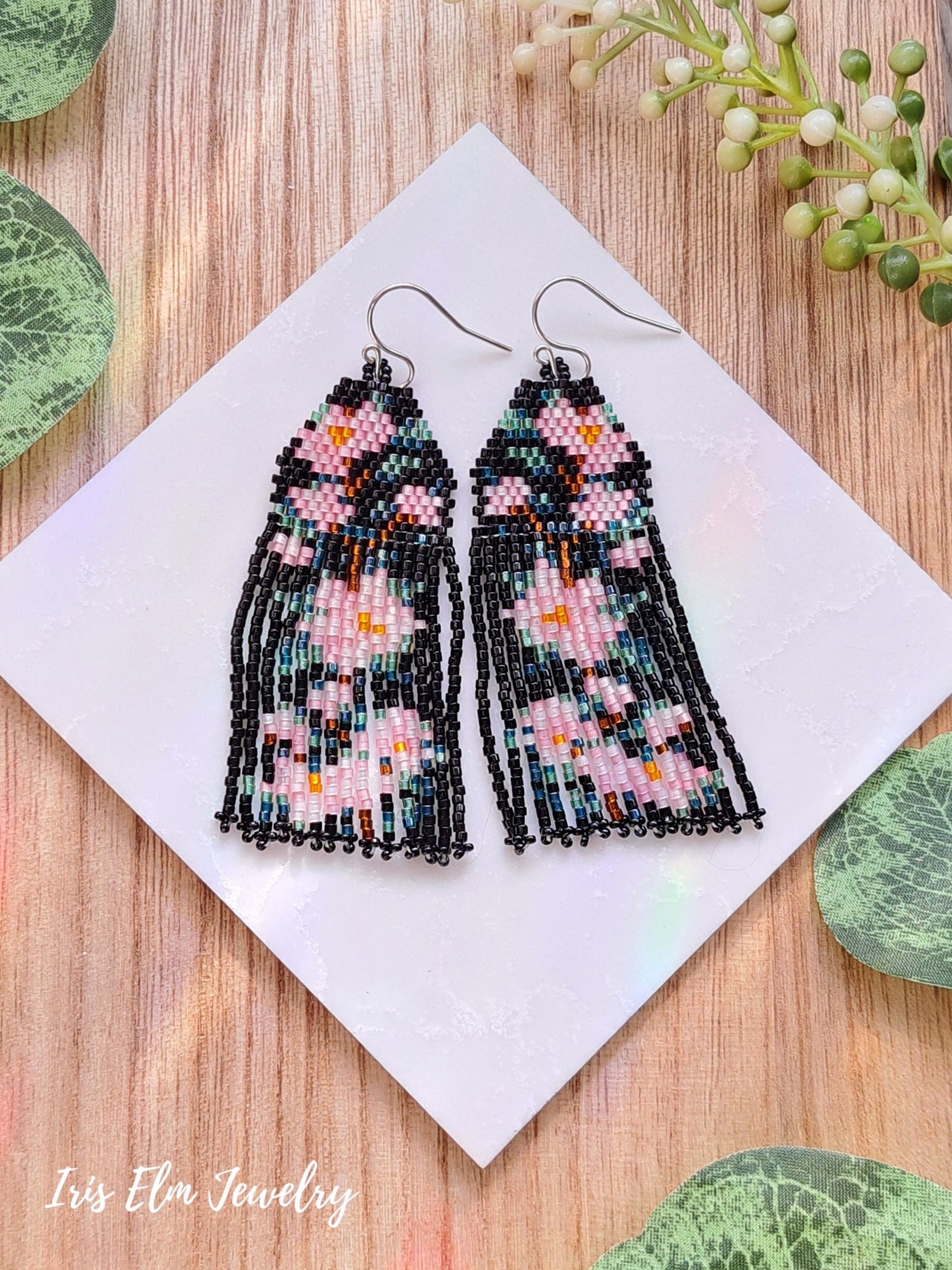 Beaded black and pink cherry blossom flower seed bead fringe earrings with floral pattern on a white card, surrounded by green leaves.