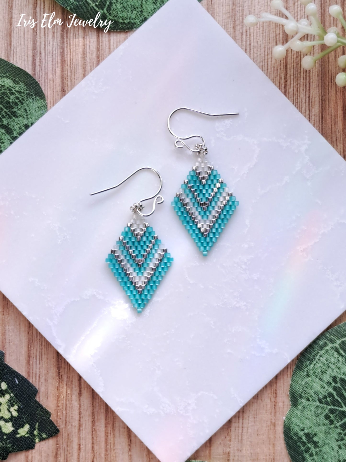 mint green striped seed bead diamond shape beaded earrings on a white cloth with 'Iris Ella Jewelry' branding.