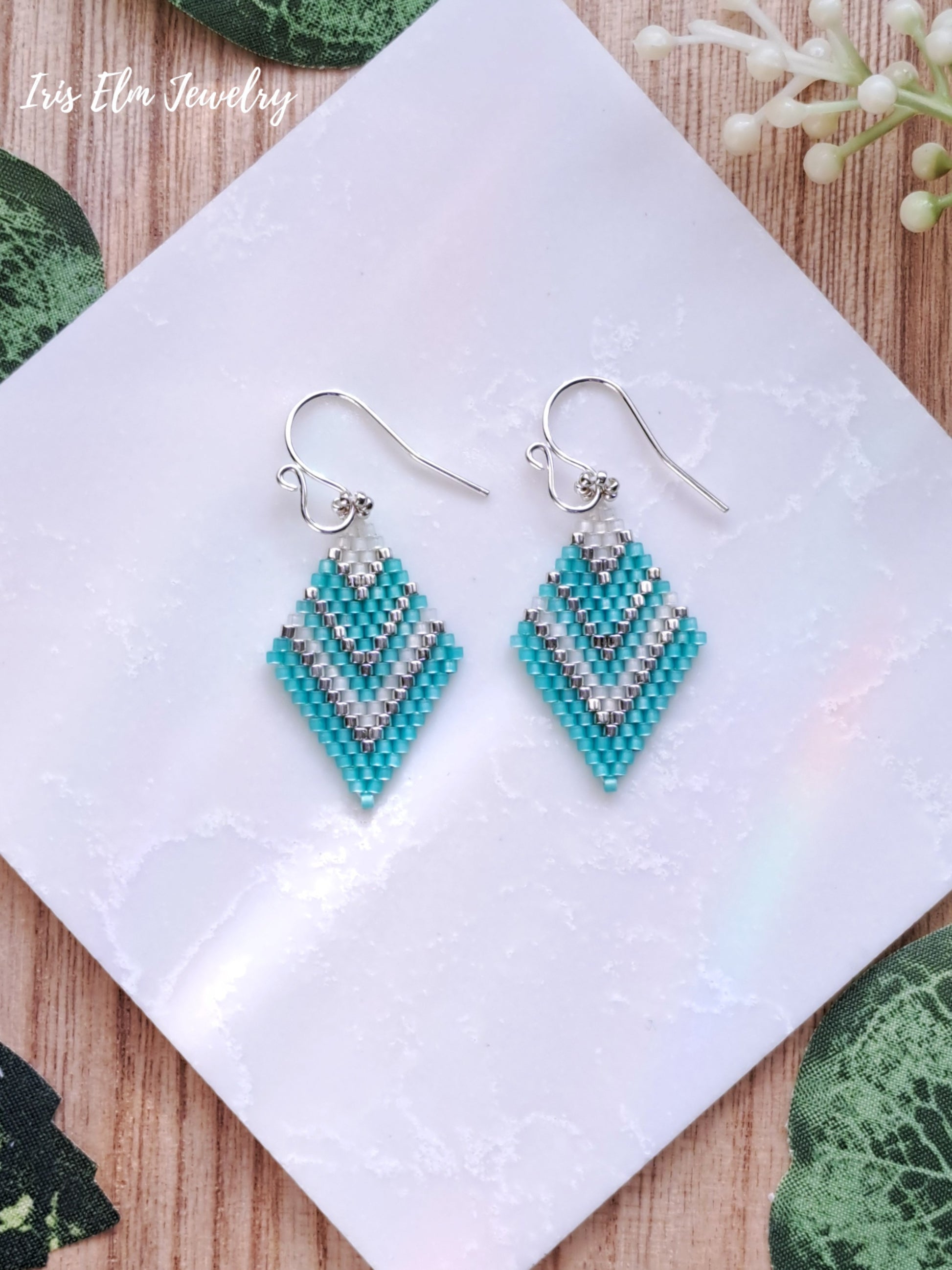 mint green and white diamond shape seed bead earrings on a white cloth with a natural background