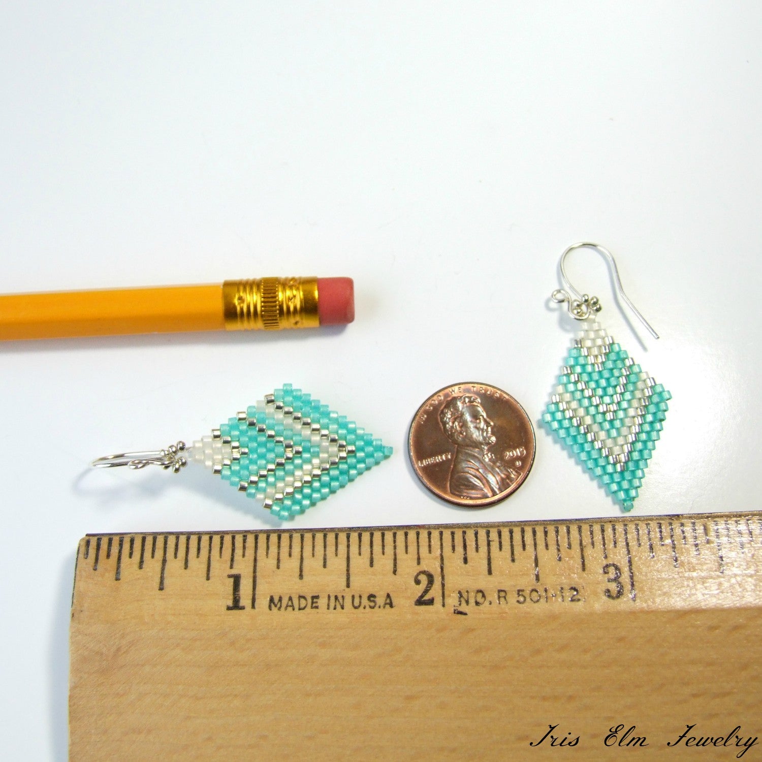 Beaded earrings next to a pencil, penny, and ruler for scale on a white background