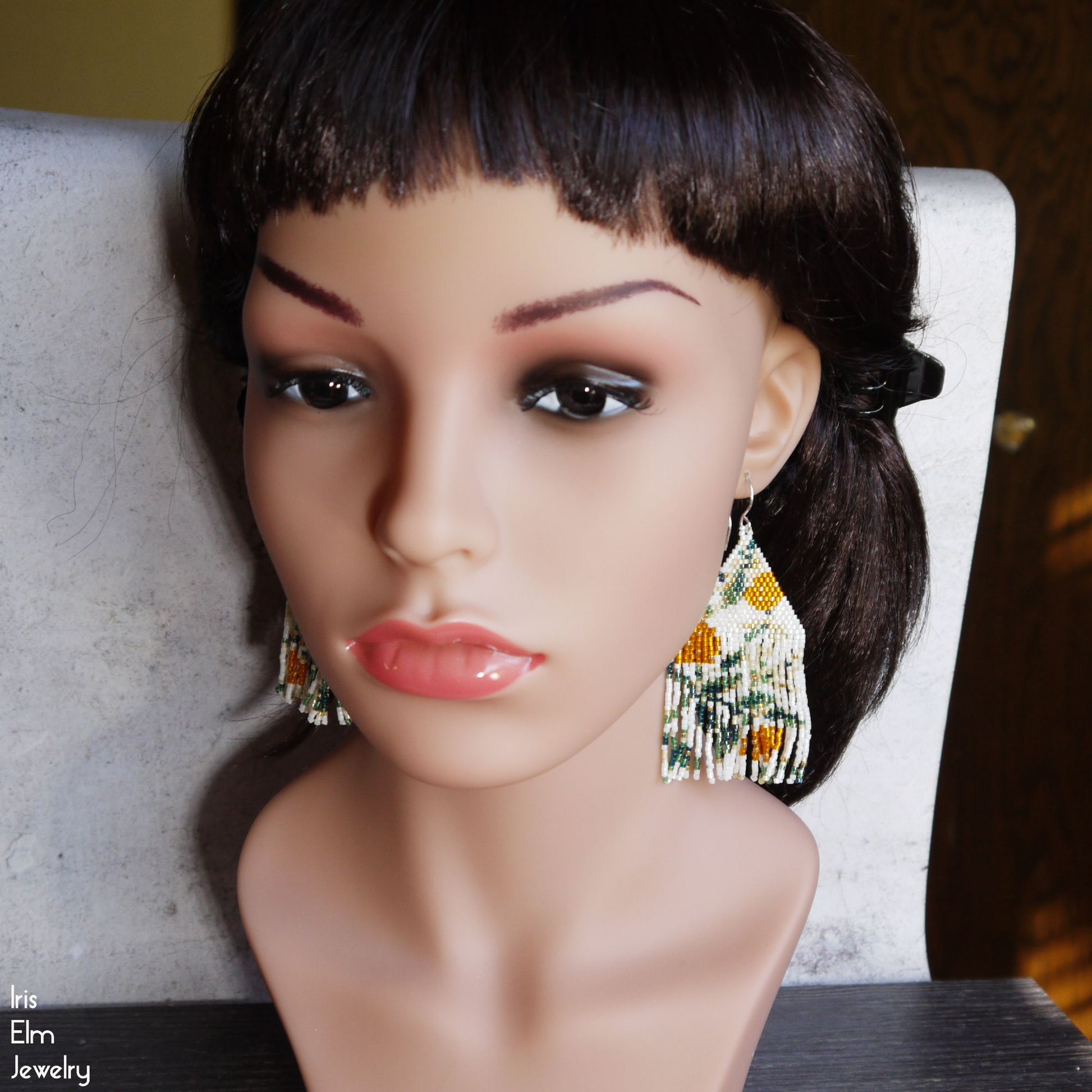 Mannequin head with black hair wearing colorful orange flower fringe earrings on a blurred background