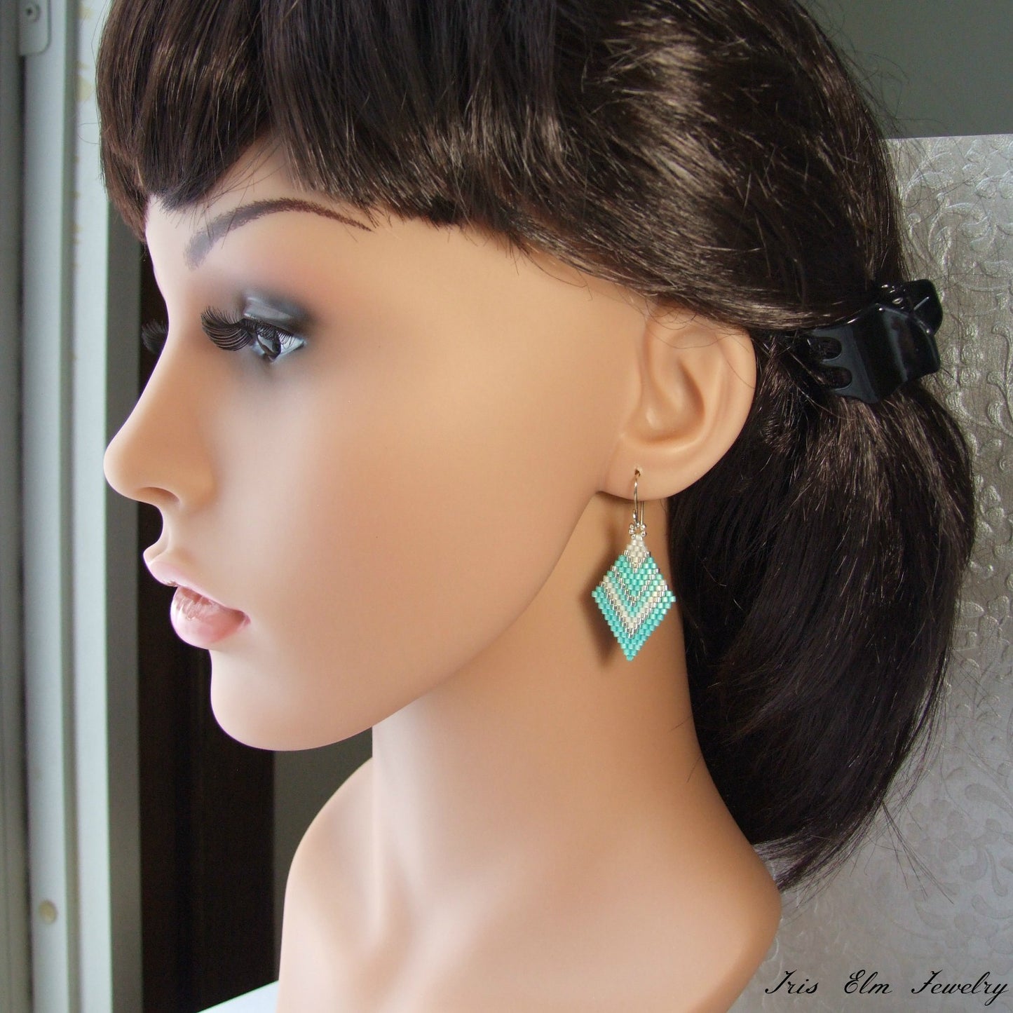 Mannequin head with dark hair styled in a ponytail, wearing mint green diamond shape seed bead earrings.