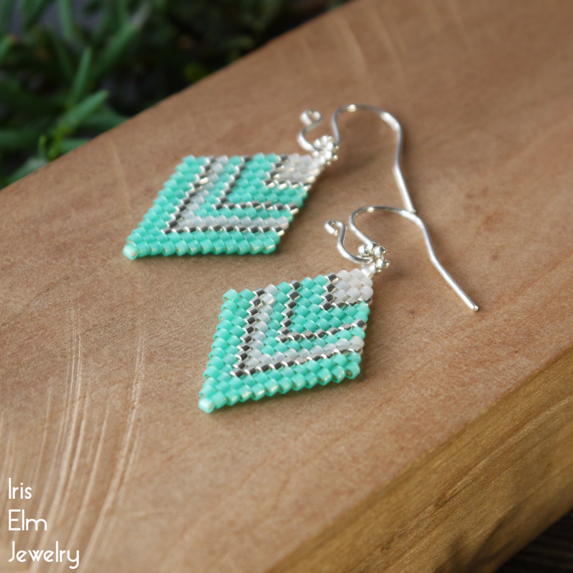 mint green and silver chevron patterned diamond shape seed bead earrings on a wooden surface with 'Iris Elm Jewelry' branding.