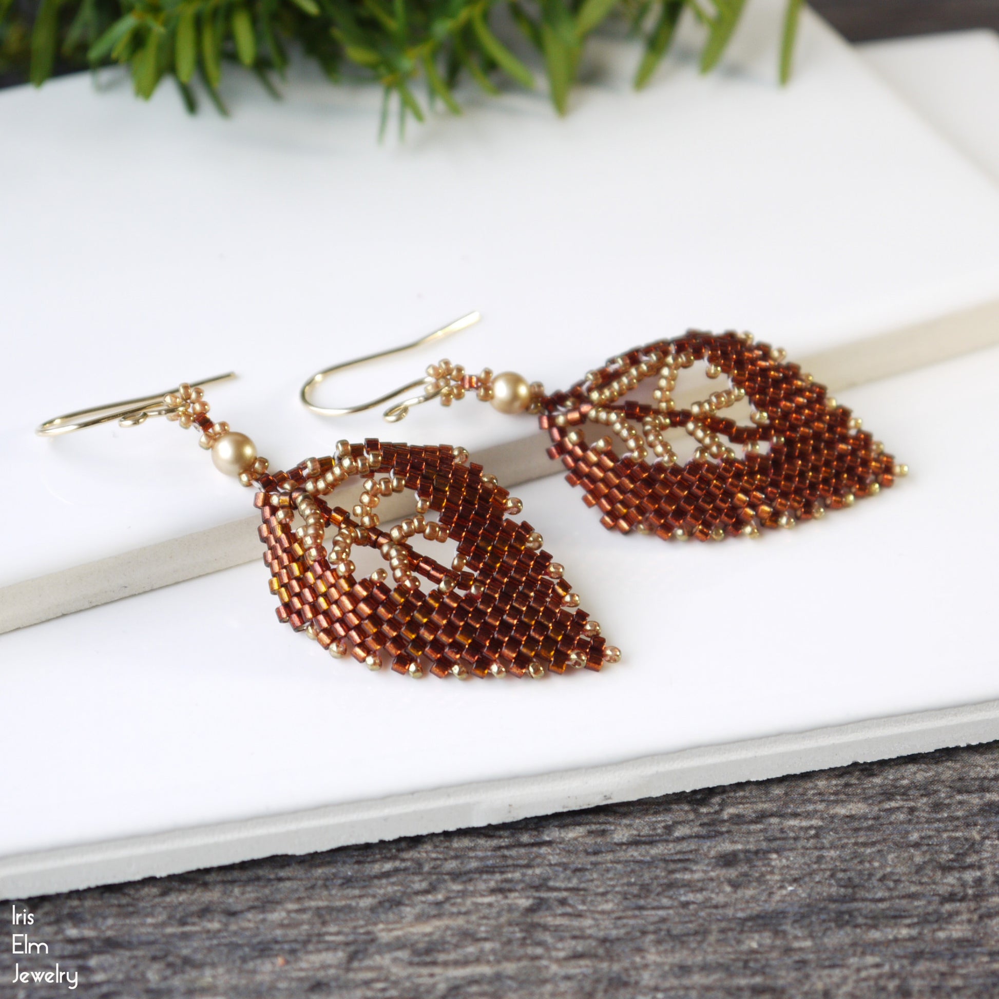 Autumn Leaf-shaped beaded seed bead earrings on a white surface with greenery in the background