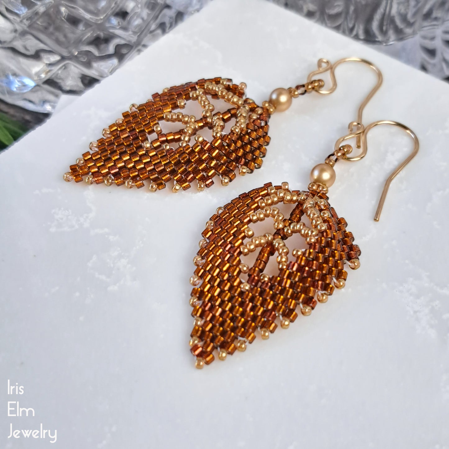 Pair of gold and topaz brown beaded leaf earrings on a white surface with 'Iris Elm Jewelry' branding.