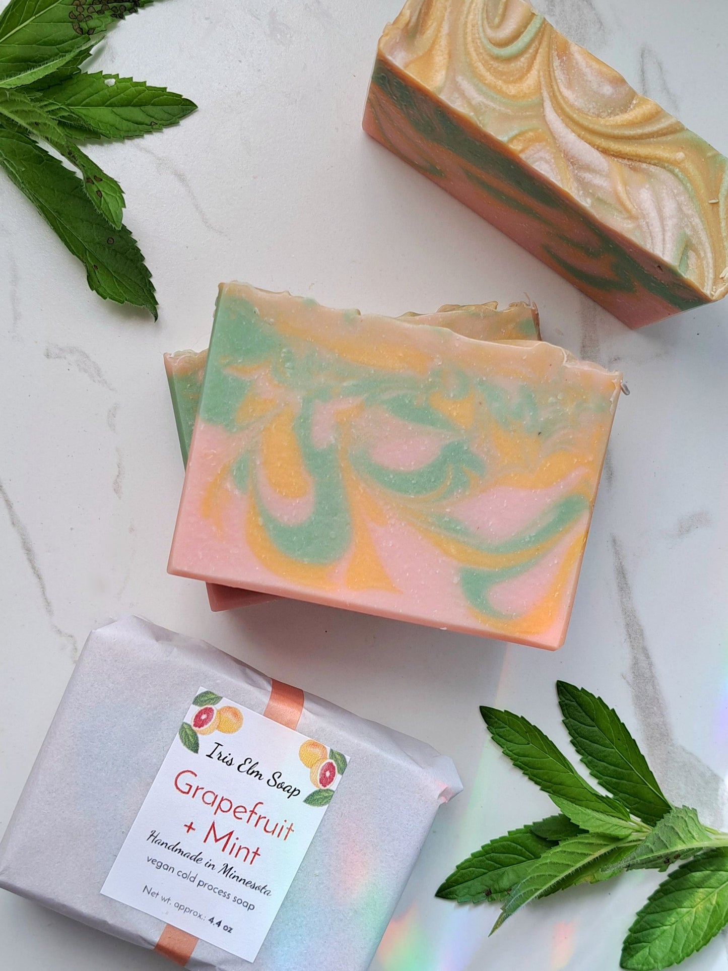 Handmade soap bars with grapefruit and mint scent on a light surface with green leaves.