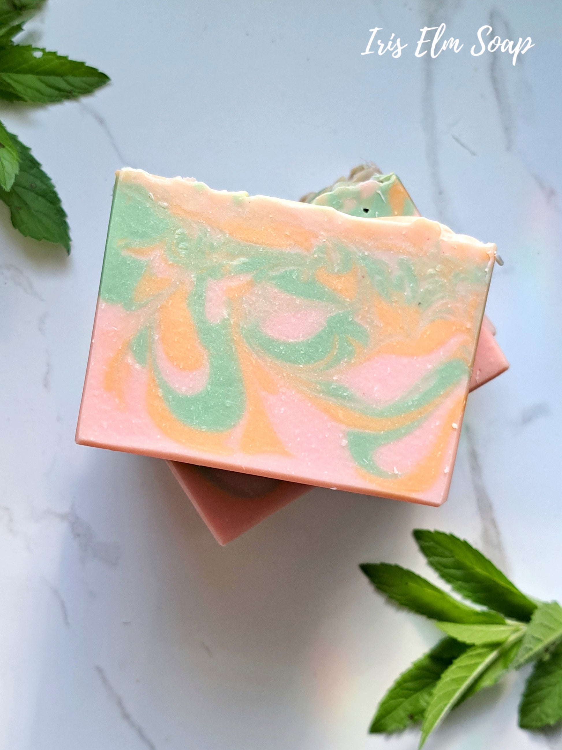 Colorful grapefruit and mint handmade soap bar with green leaves on a light background