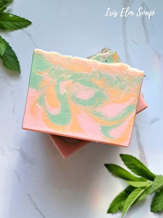 Colorful grapefruit and mint handmade soap bar with green leaves on a light background