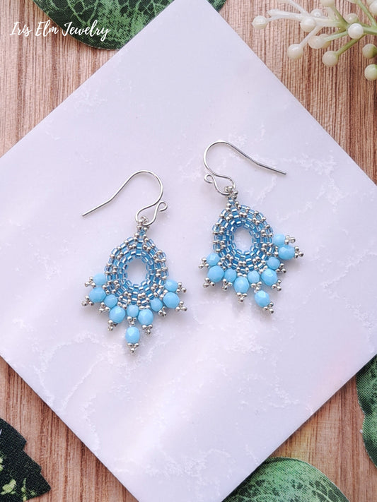 Pair of blue beaded glass fan earrings on a white card with a natural background