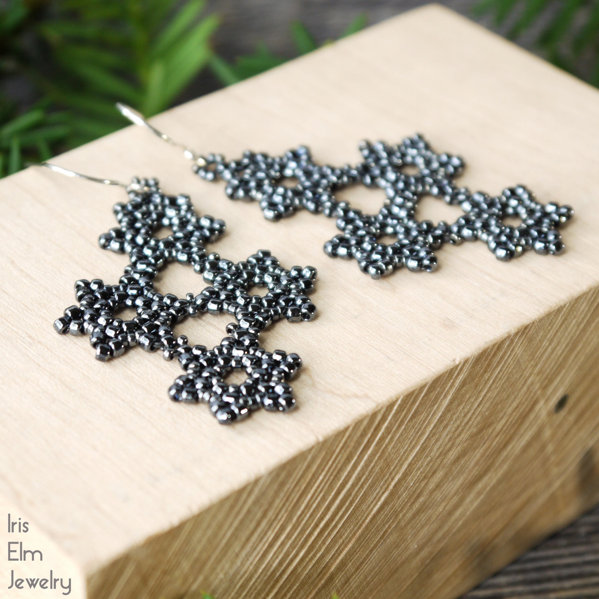 Decorative beadwork grey earrings on a wooden block with 'Iris Elm Jewelry' branding.