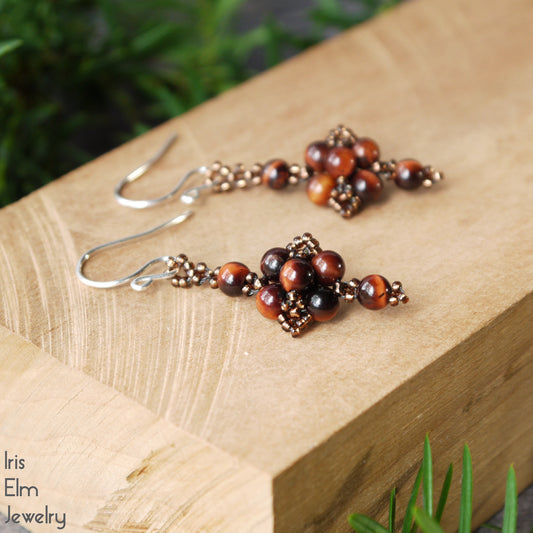 Pair of beadwork tiger eye earrings on a wooden surface with 'Iris Elm Jewelry' branding.