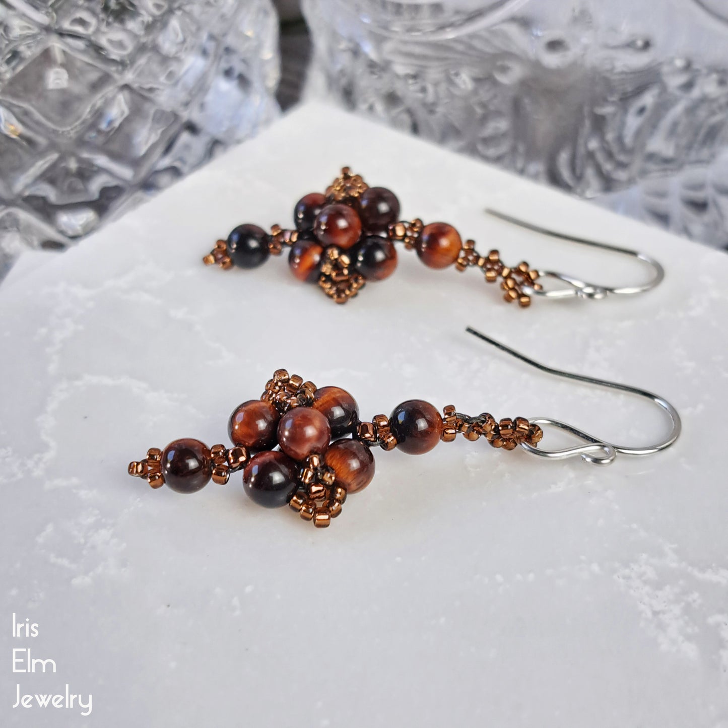 Pair of beaded brown red tiger eye earrings on a white surface with 'Iris Elm Jewelry' branding.