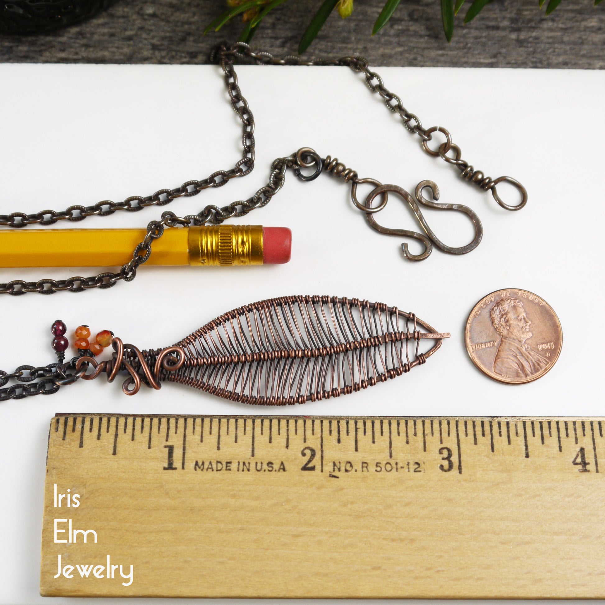 3 inch pendant with a leaf design next to a ruler, pencil, and penny on a white surface.
