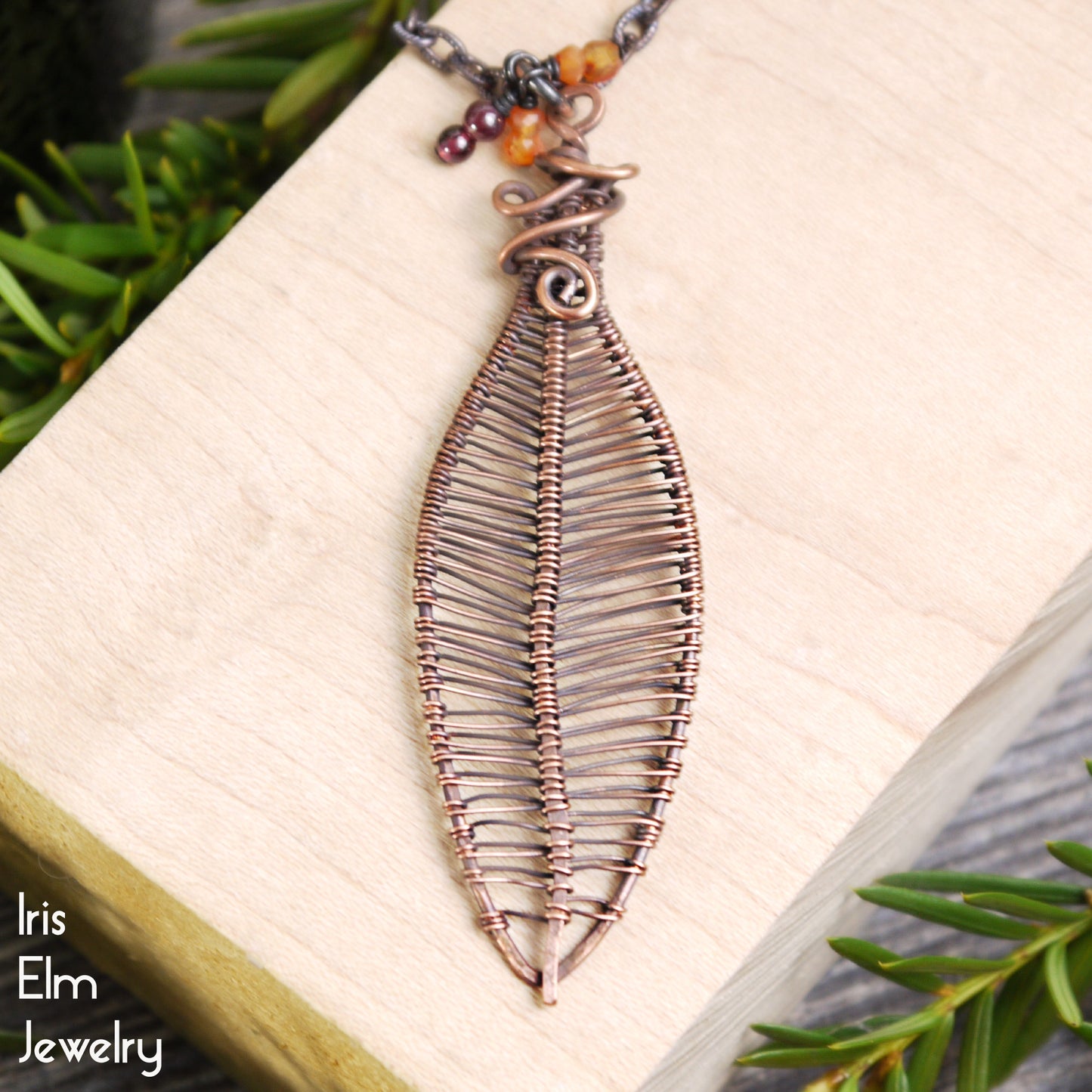 Leaf-shaped copper pendant necklace with carnelian and garnet gemstone berries on a book with green leaves