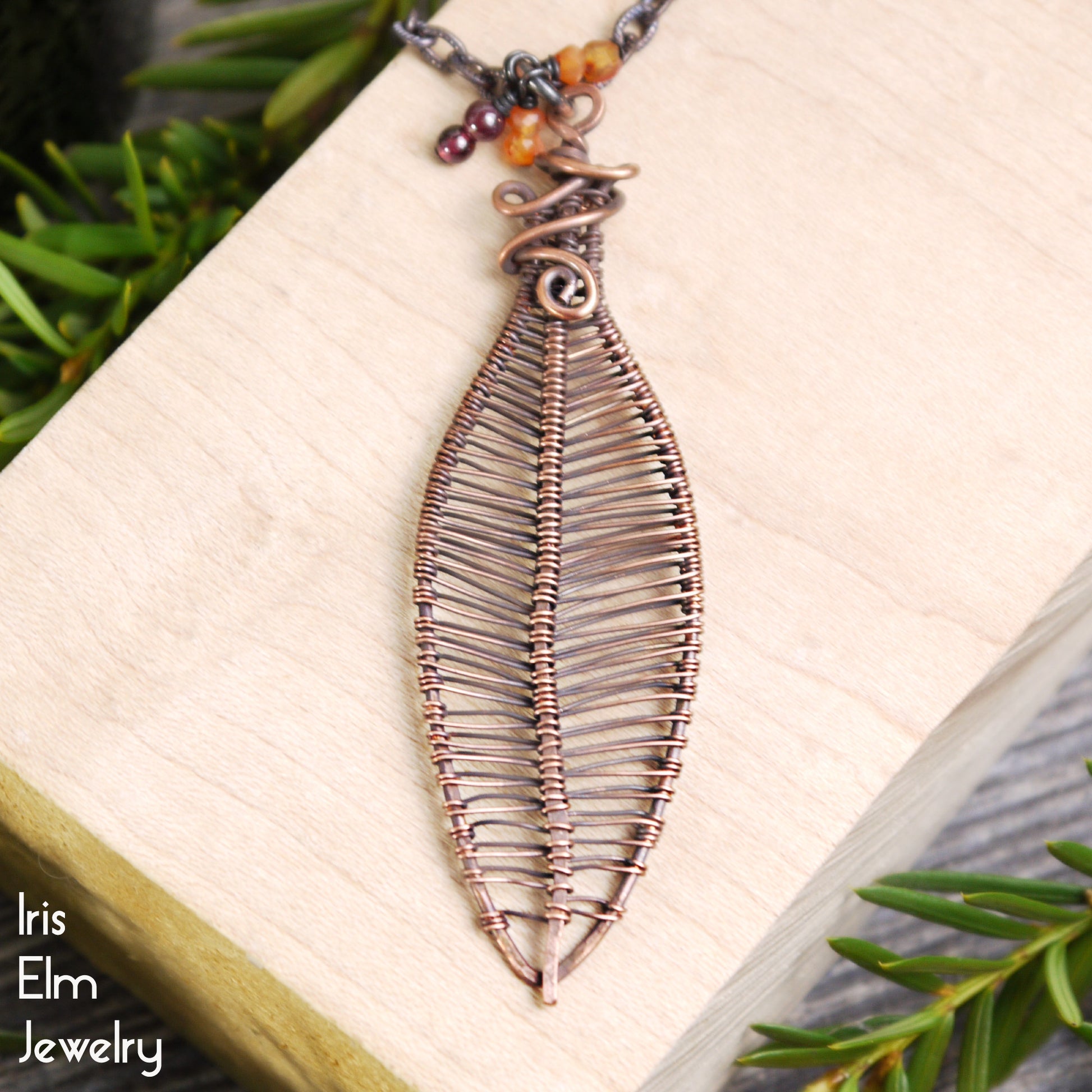 Leaf-shaped copper pendant necklace with carnelian and garnet gemstone berries on a book with green leaves